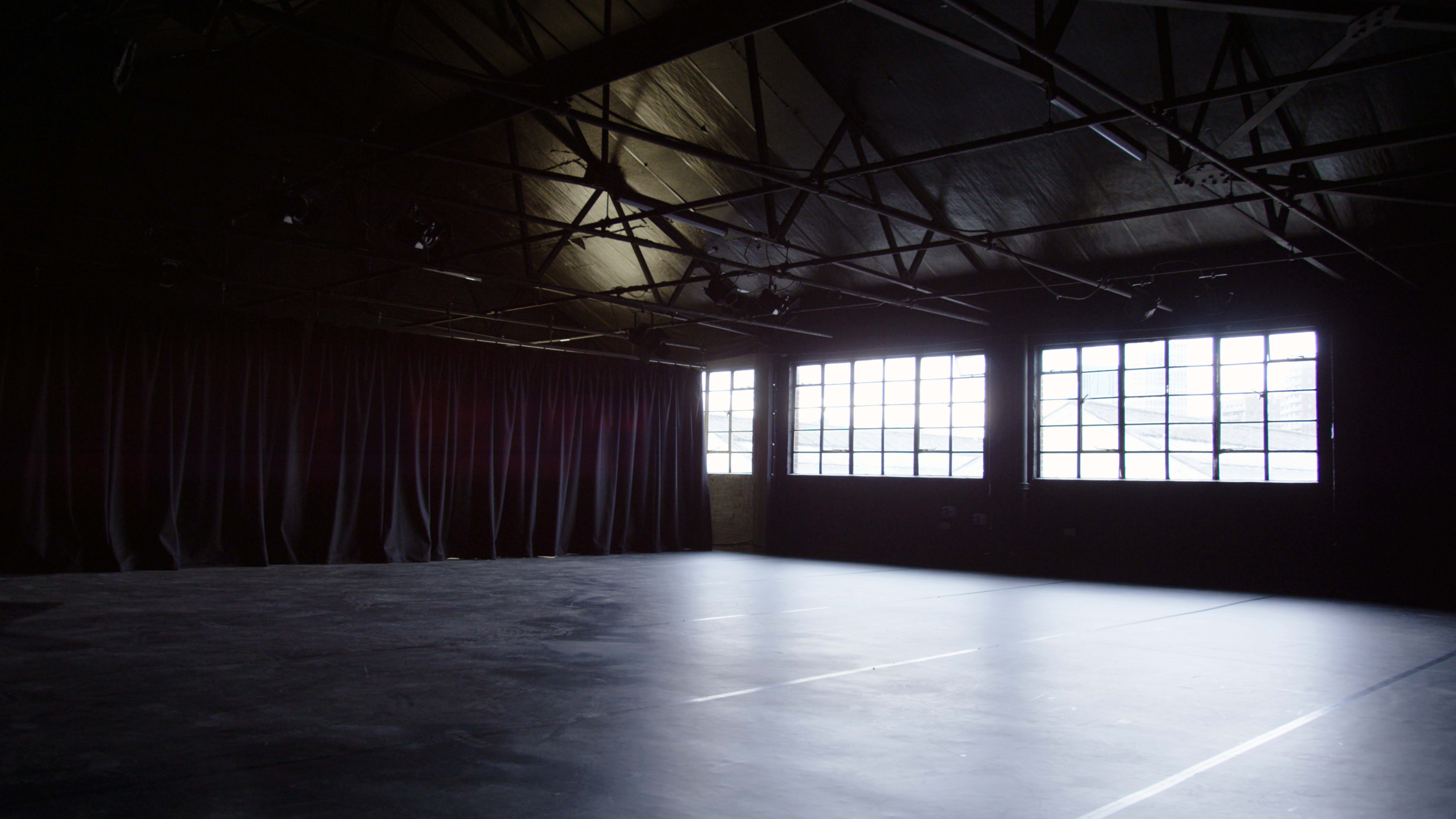 An empty stage area with large windows and dark curtains in a warehouse-like space.