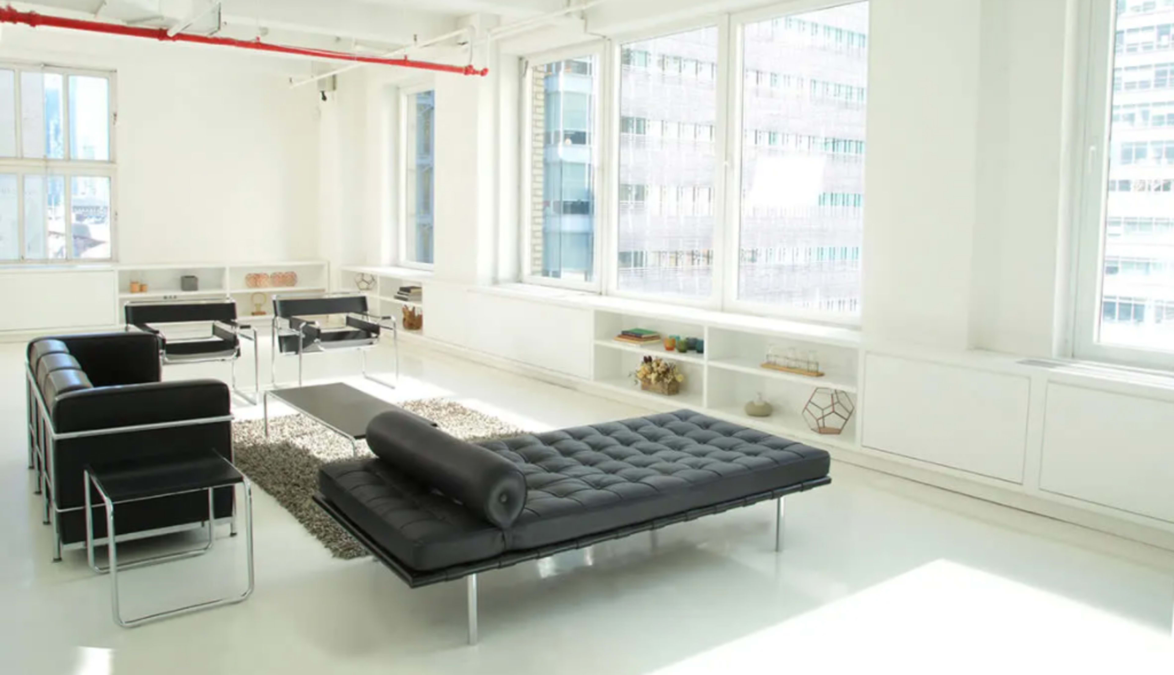 A modern, minimalist office space featuring black furniture, large windows, and a white color scheme.