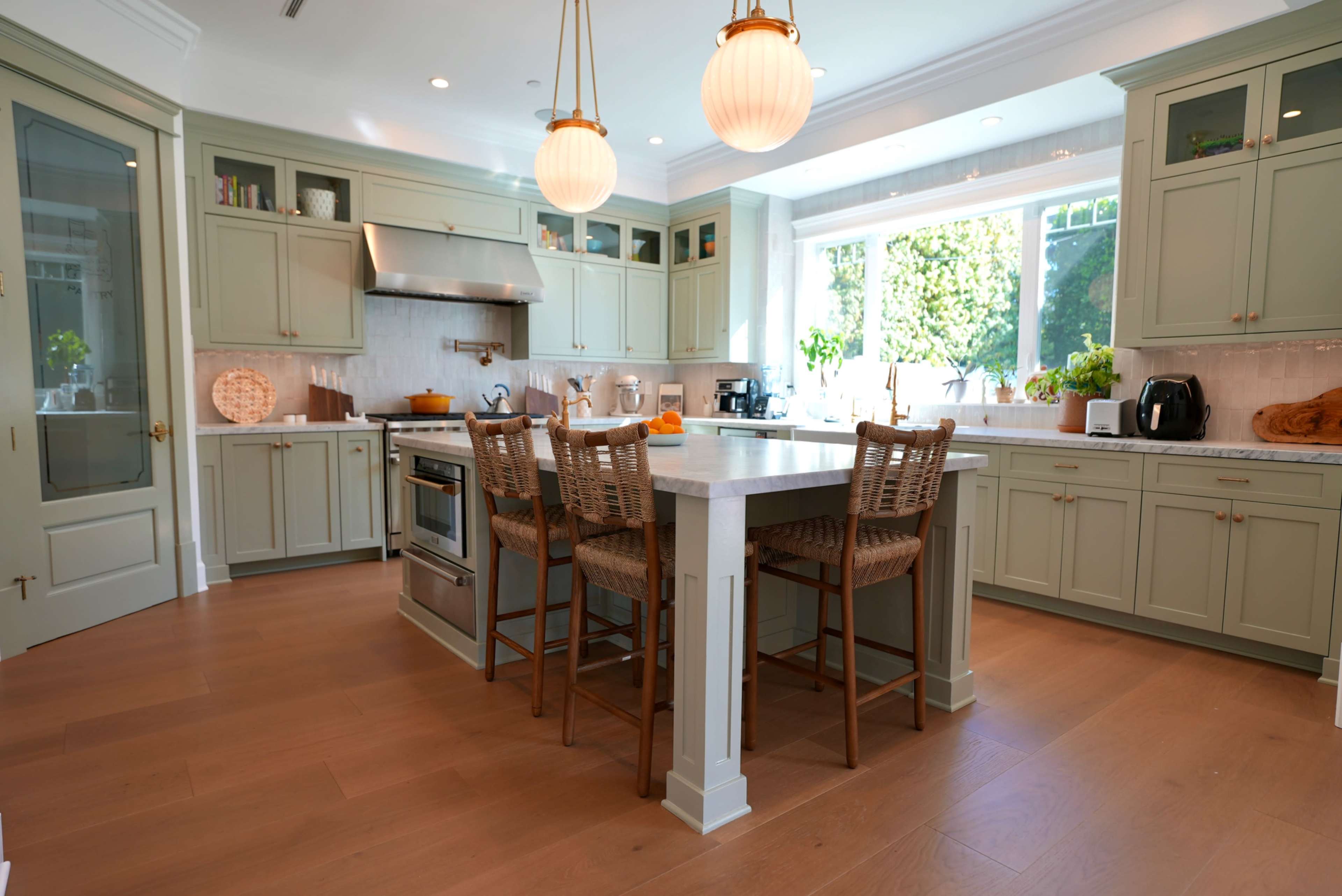 A spacious kitchen features light green cabinetry, a large central island with bar stools, and large windows that provide natural light.