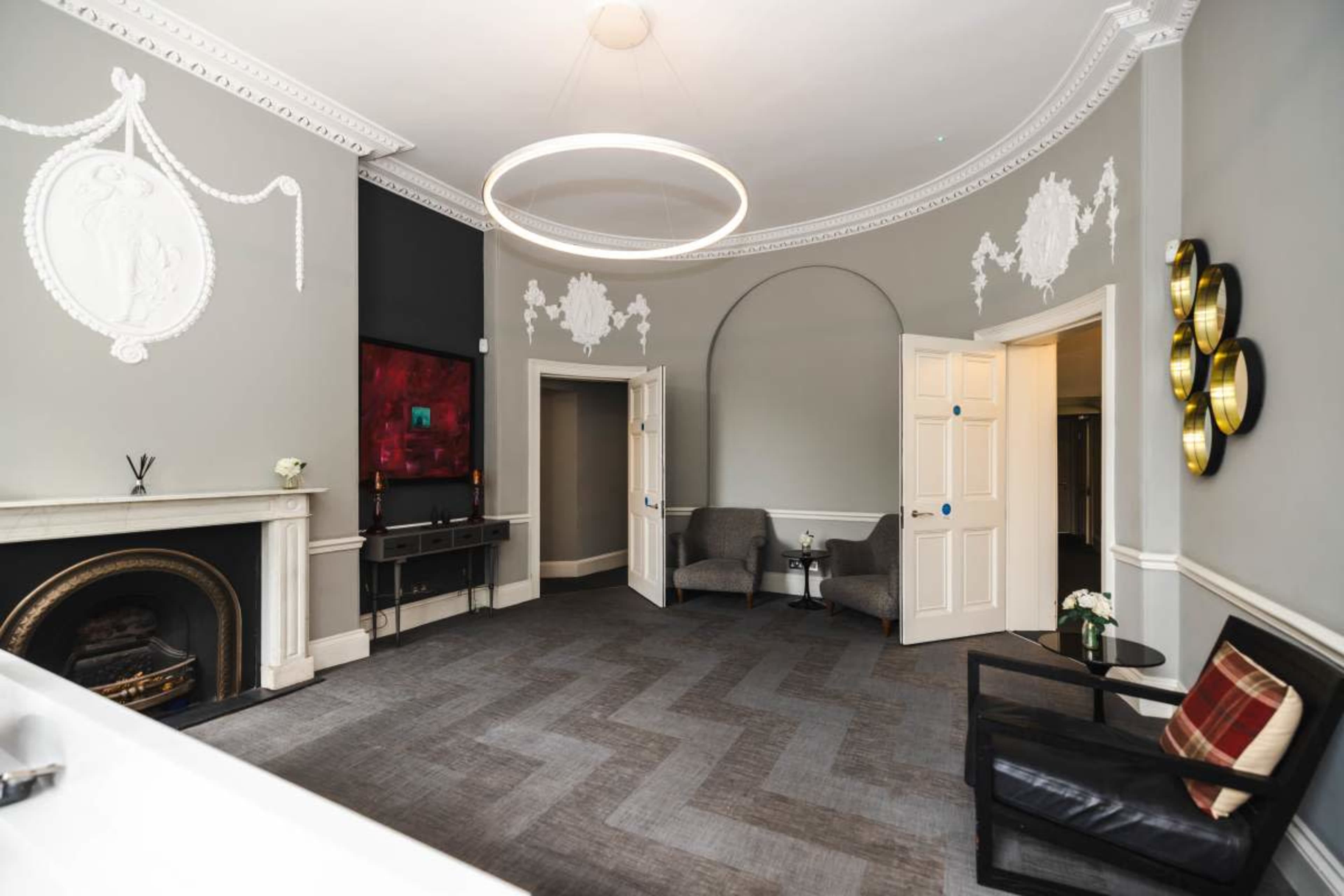 The image shows a well-decorated interior space featuring a fireplace, two armchairs, and a circular light fixture hanging from the ceiling.