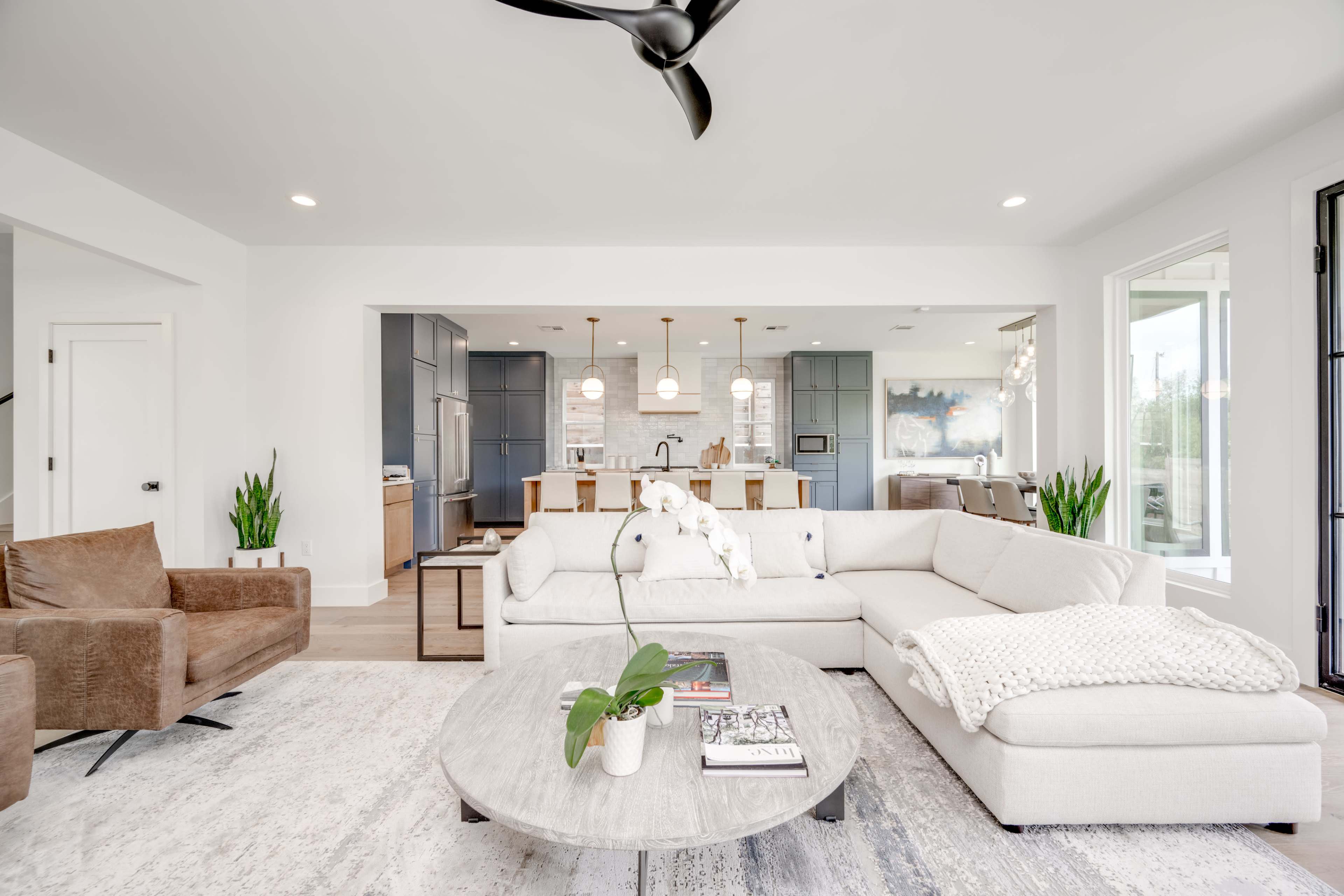 The image shows a modern living room featuring a sectional sofa, coffee table, and open access to a kitchen in the background.