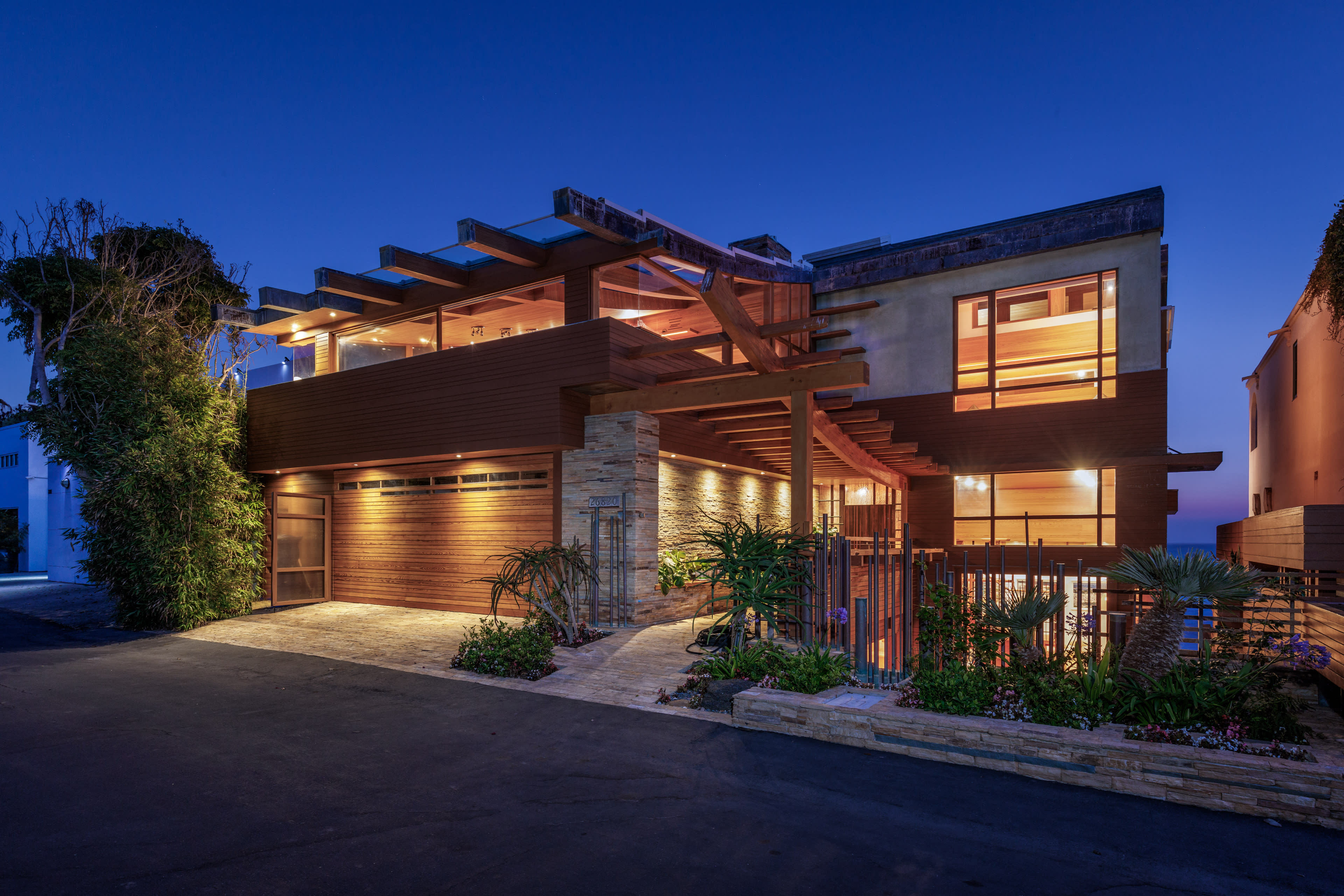 A modern multi-level house with a wooden facade and large windows, illuminated against a twilight sky.