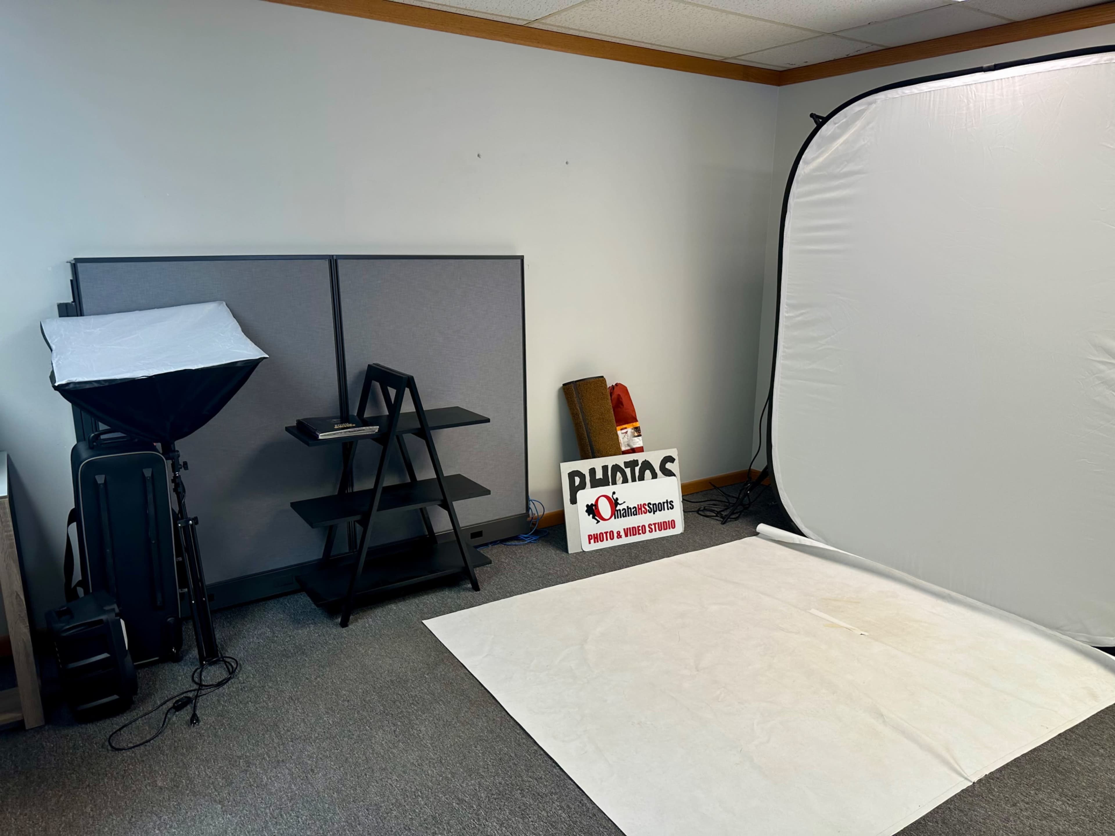The image shows a well-lit studio space featuring a backdrop, light equipment, a folding table, and a sign for a photography and video studio.