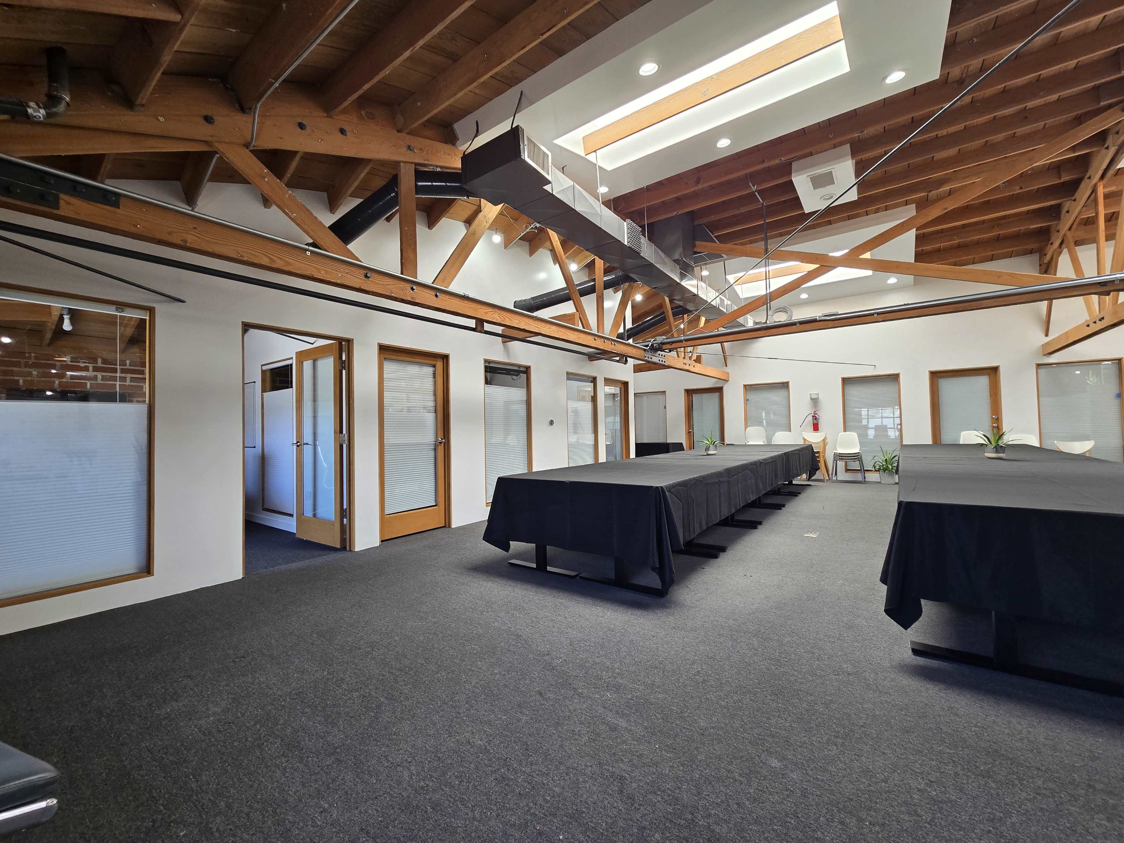 The image shows a spacious conference room with a black carpet, long tables covered in black cloth, and wooden beams visible on the ceiling.