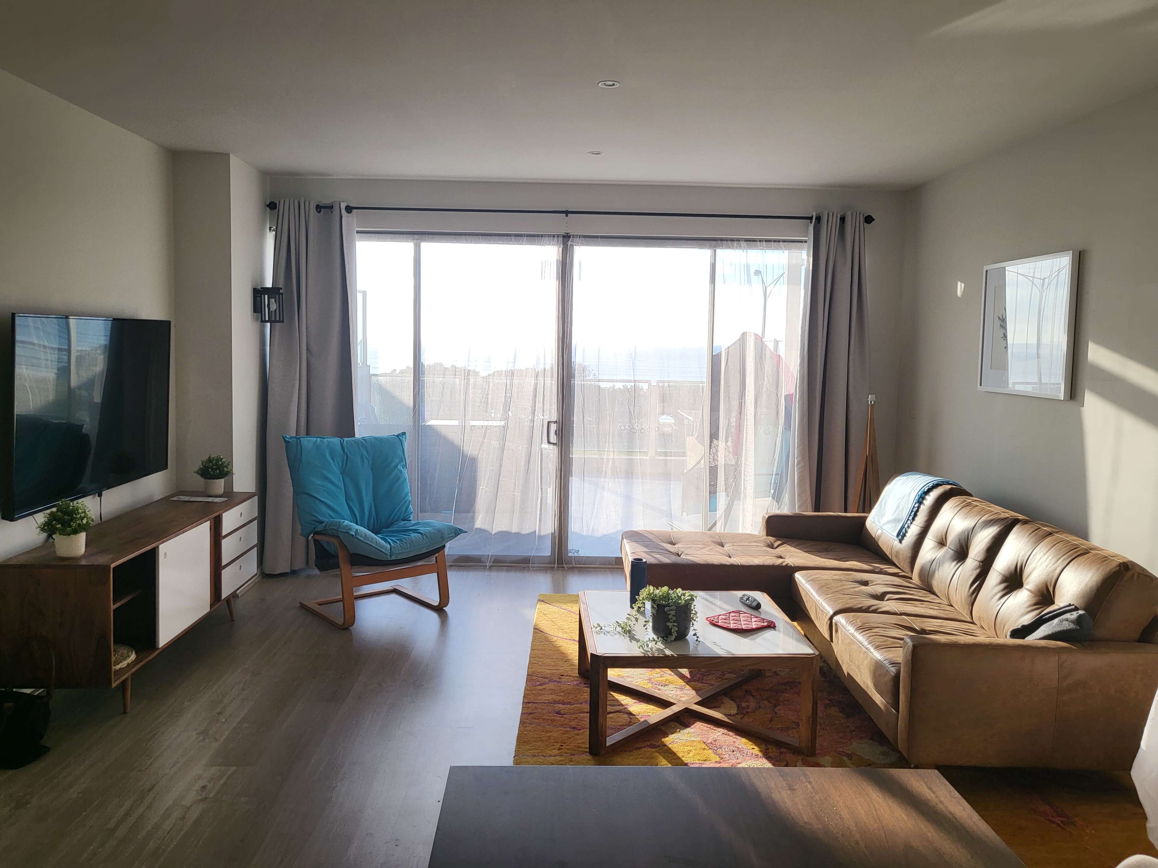 A living room features a brown sofa, a wooden coffee table, a blue chair, and large sliding glass doors leading to an outdoor area.
