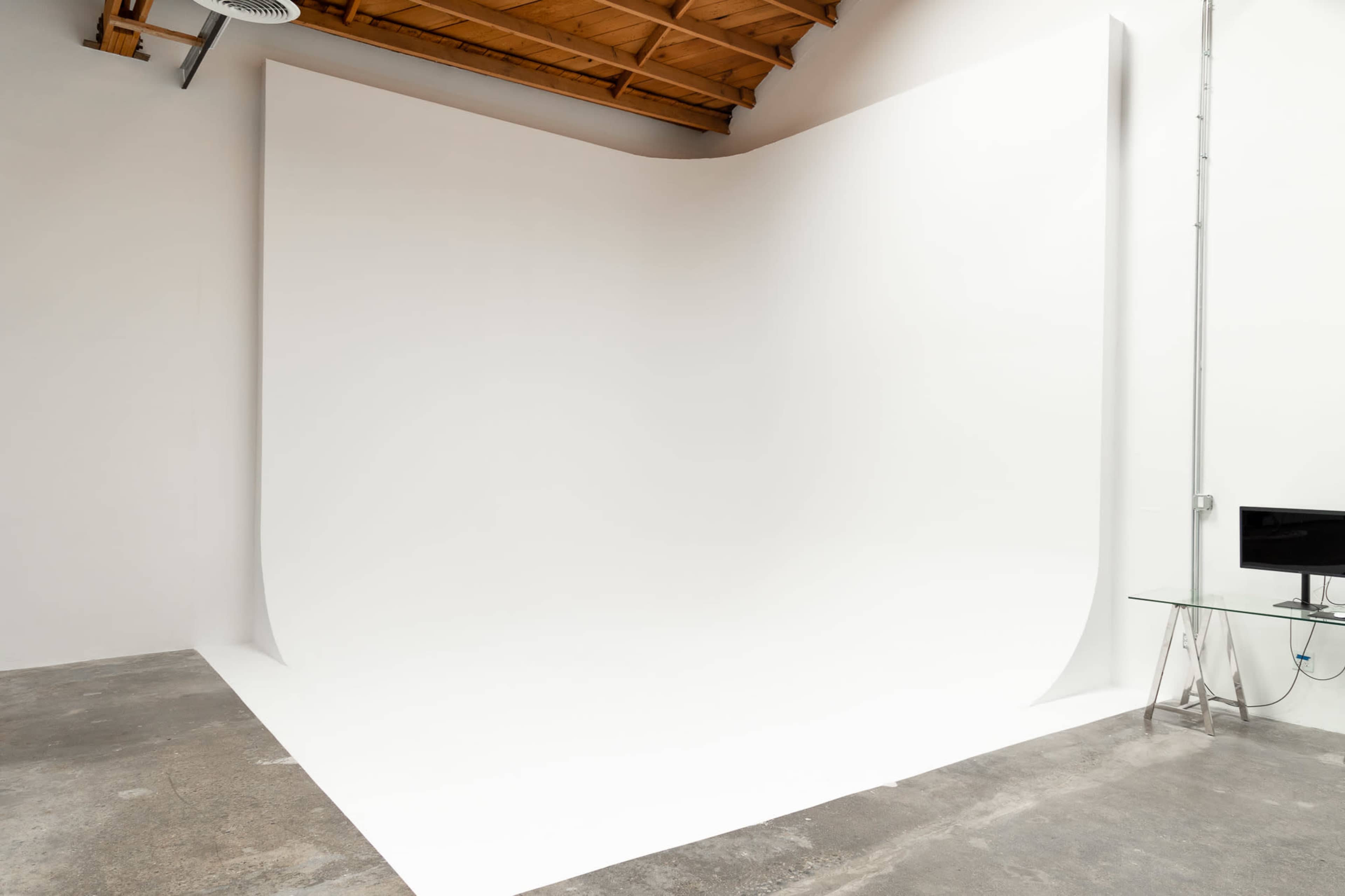 An empty studio space with a large, seamless white backdrop against a concrete floor.