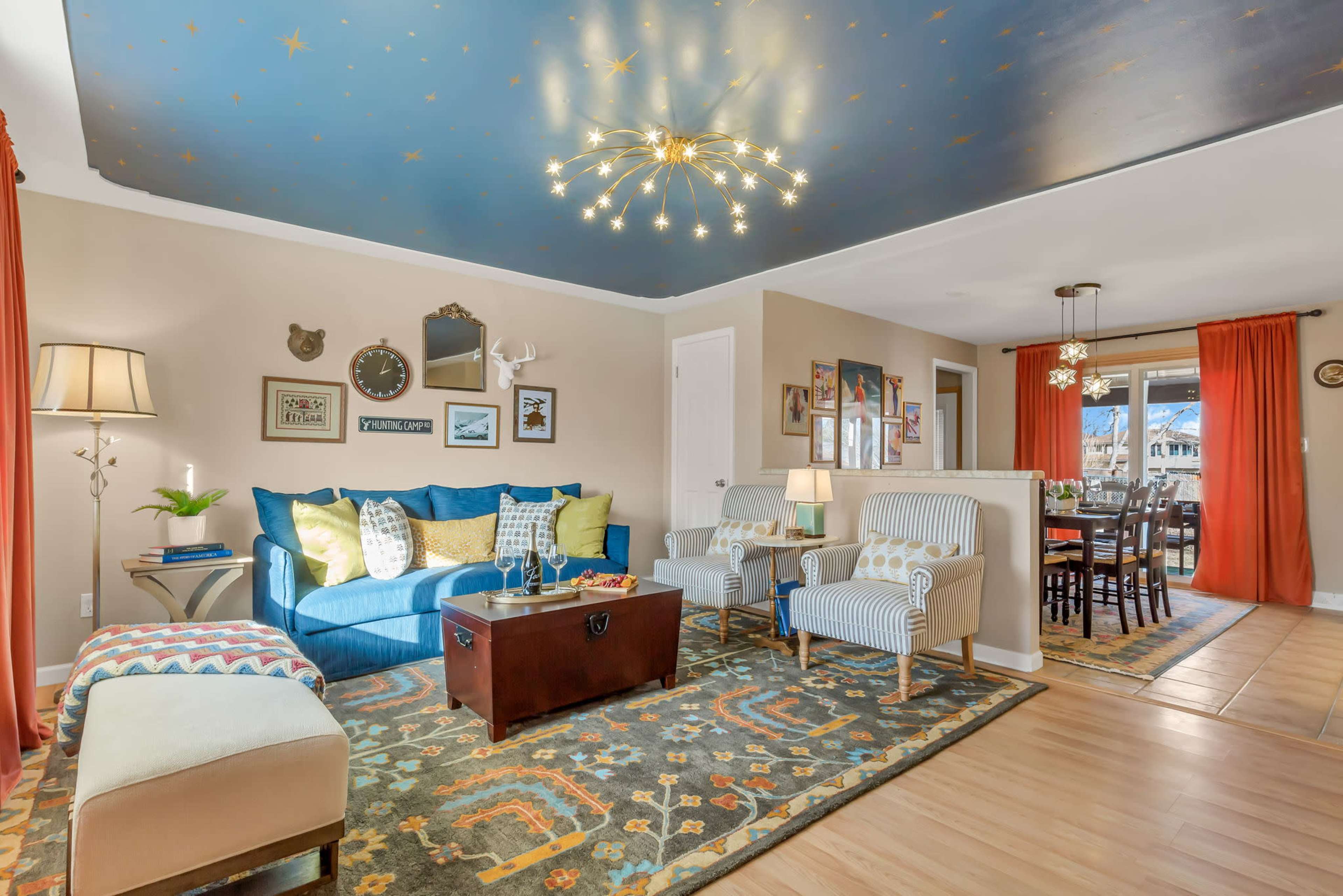 The living room features a blue sofa, patterned area rug, a wooden coffee table, and a dining area with a view through sliding glass doors.