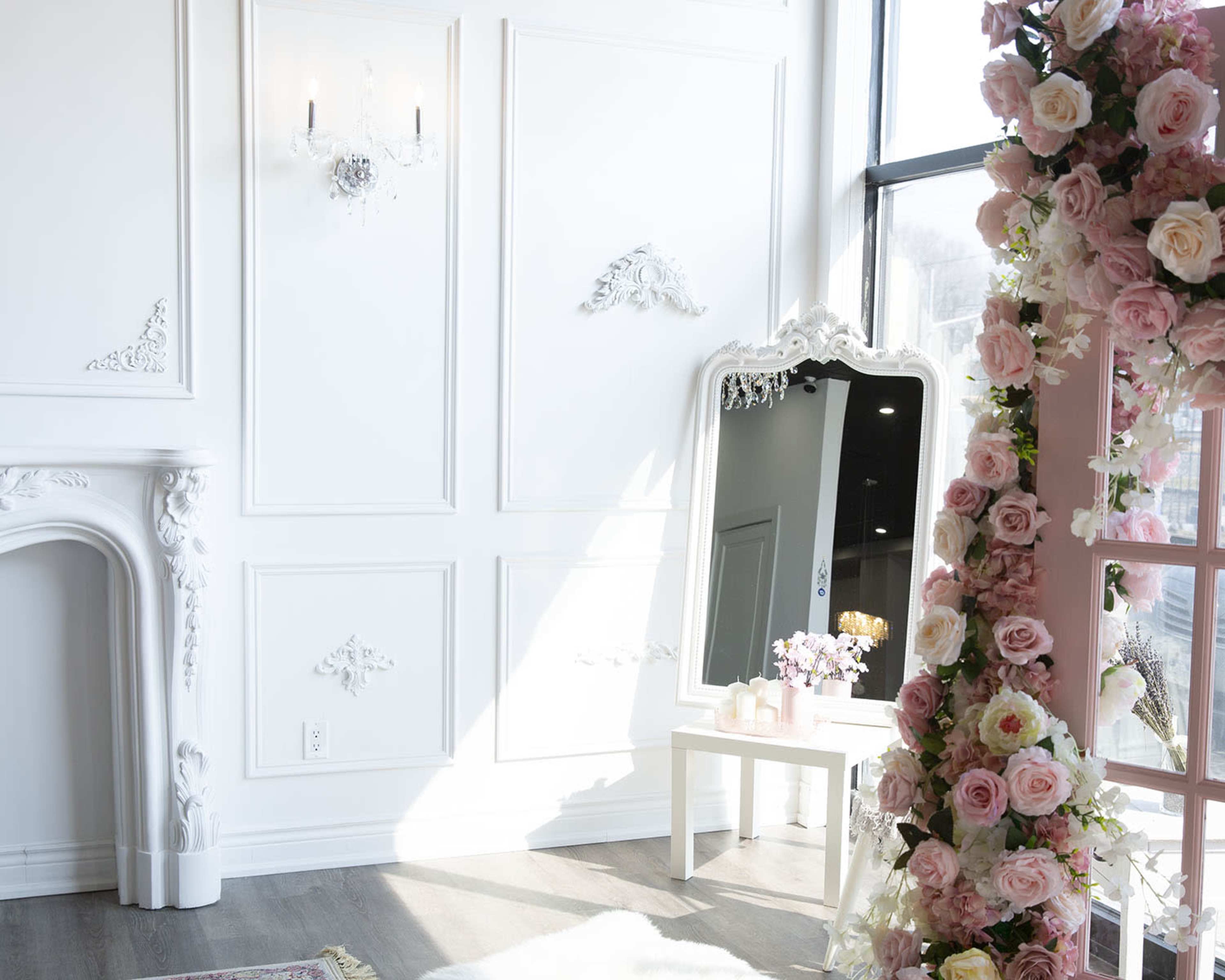 A brightly lit room with white walls, a large ornate mirror, and floral decorations on a nearby structure.