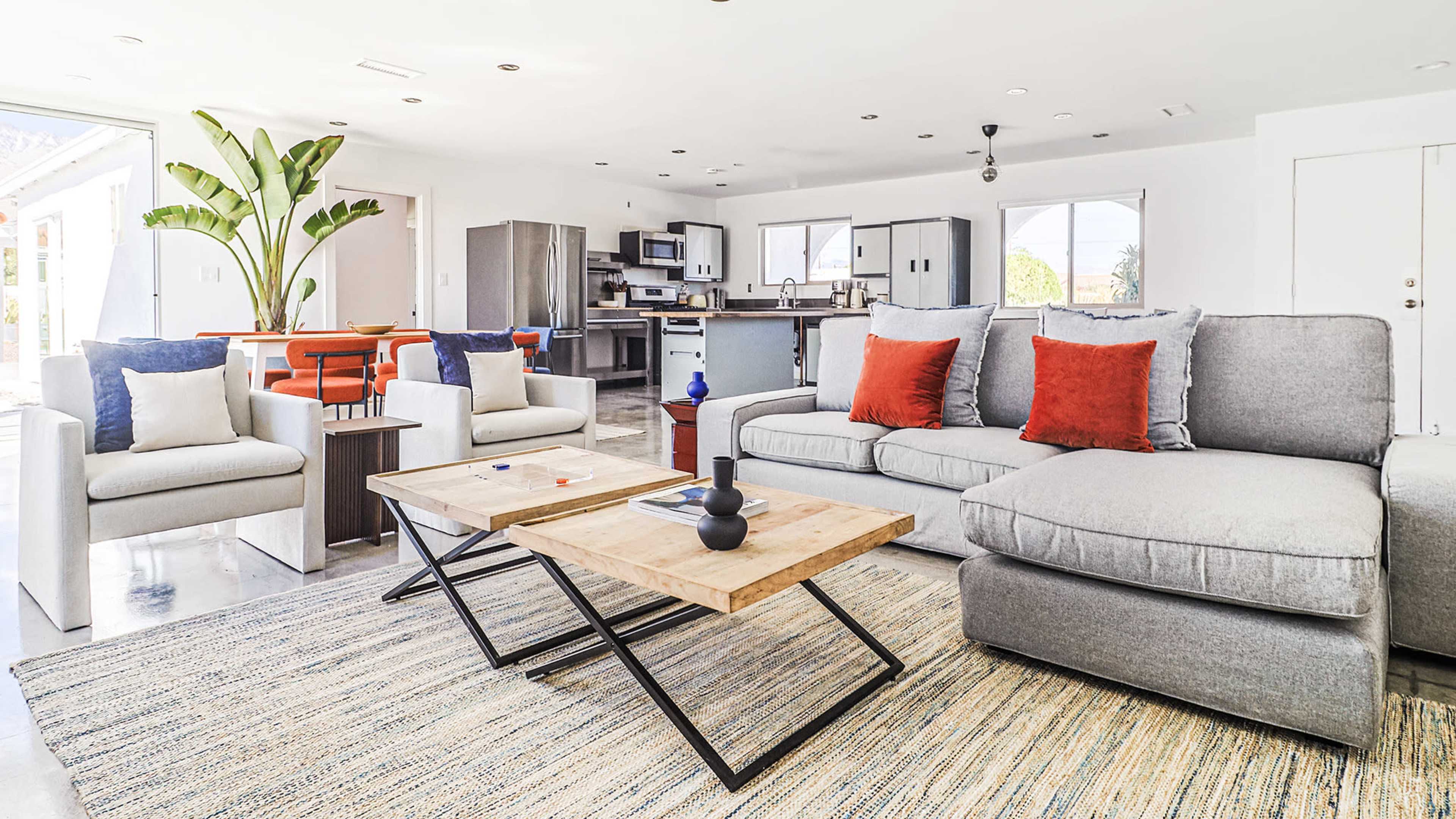 A modern living room with a gray sectional sofa, wooden coffee tables, and a dining area in an open-concept layout.