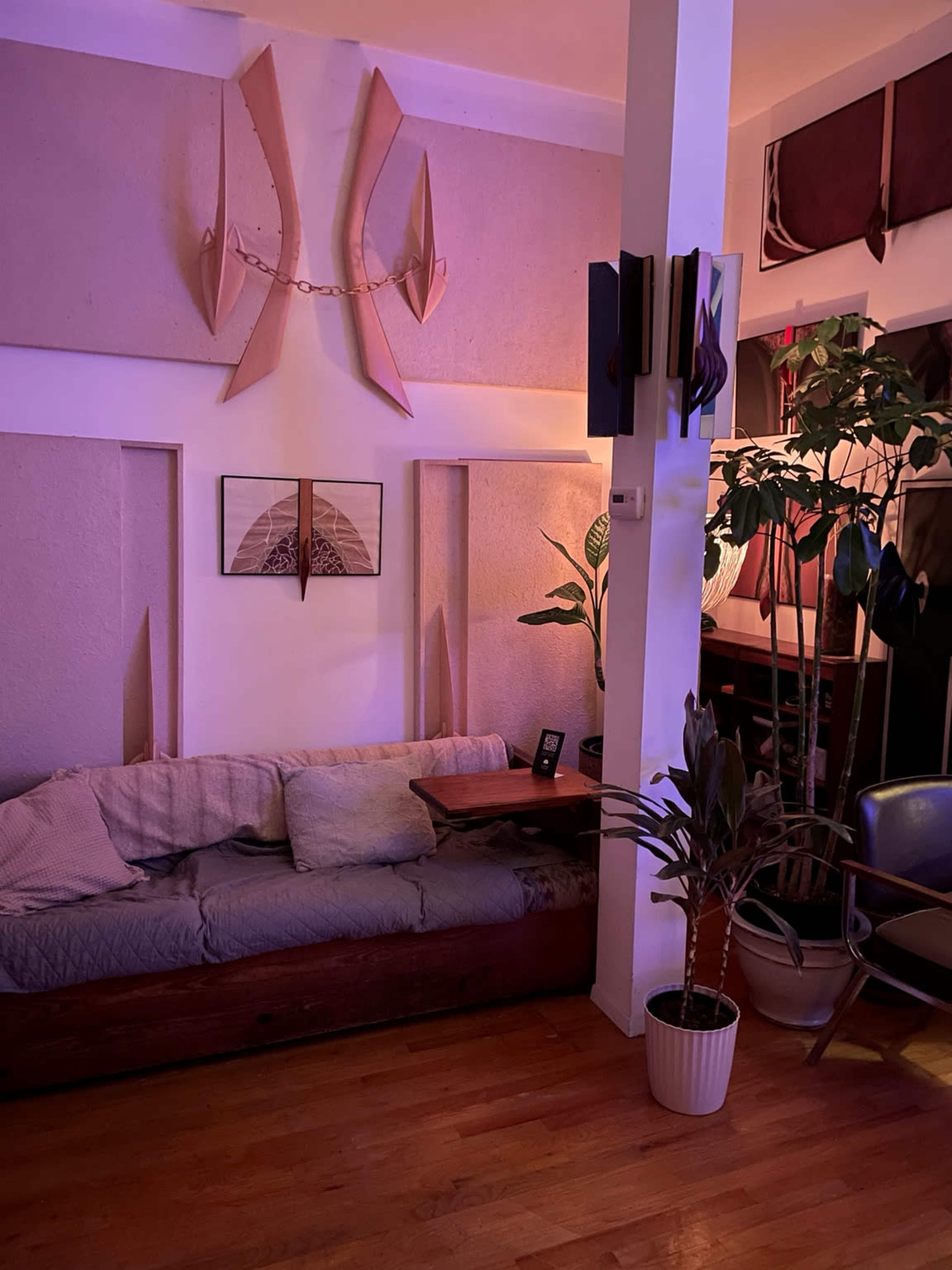 The image shows a cozy living room with a wooden sofa, decorative wall panels, a potted plant, and a small table, all illuminated by soft lighting.
