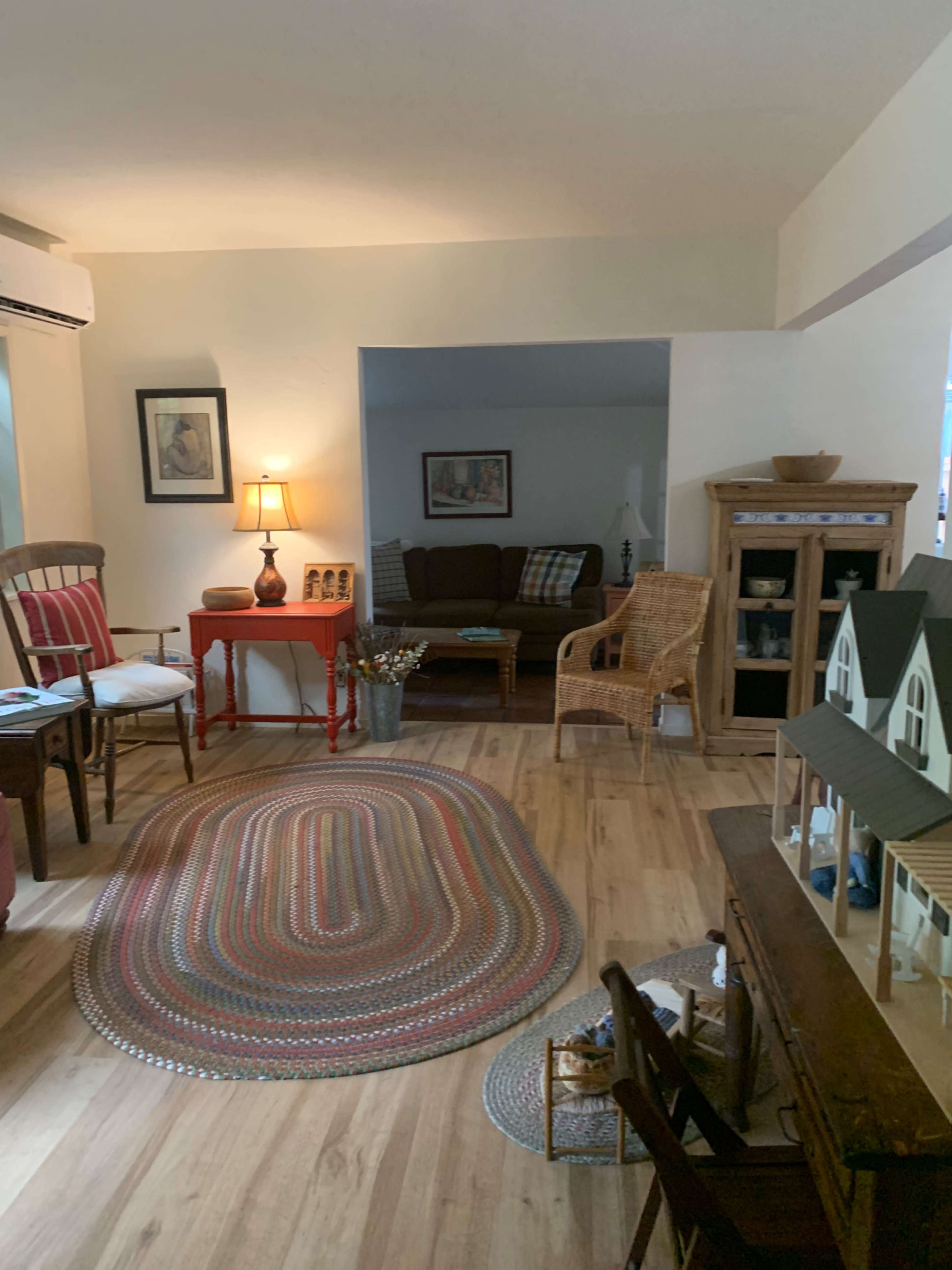 The image shows a living room featuring a seating area with a brown couch, a table lamp, and a woven rug, along with decorative furniture and a display cabinet.