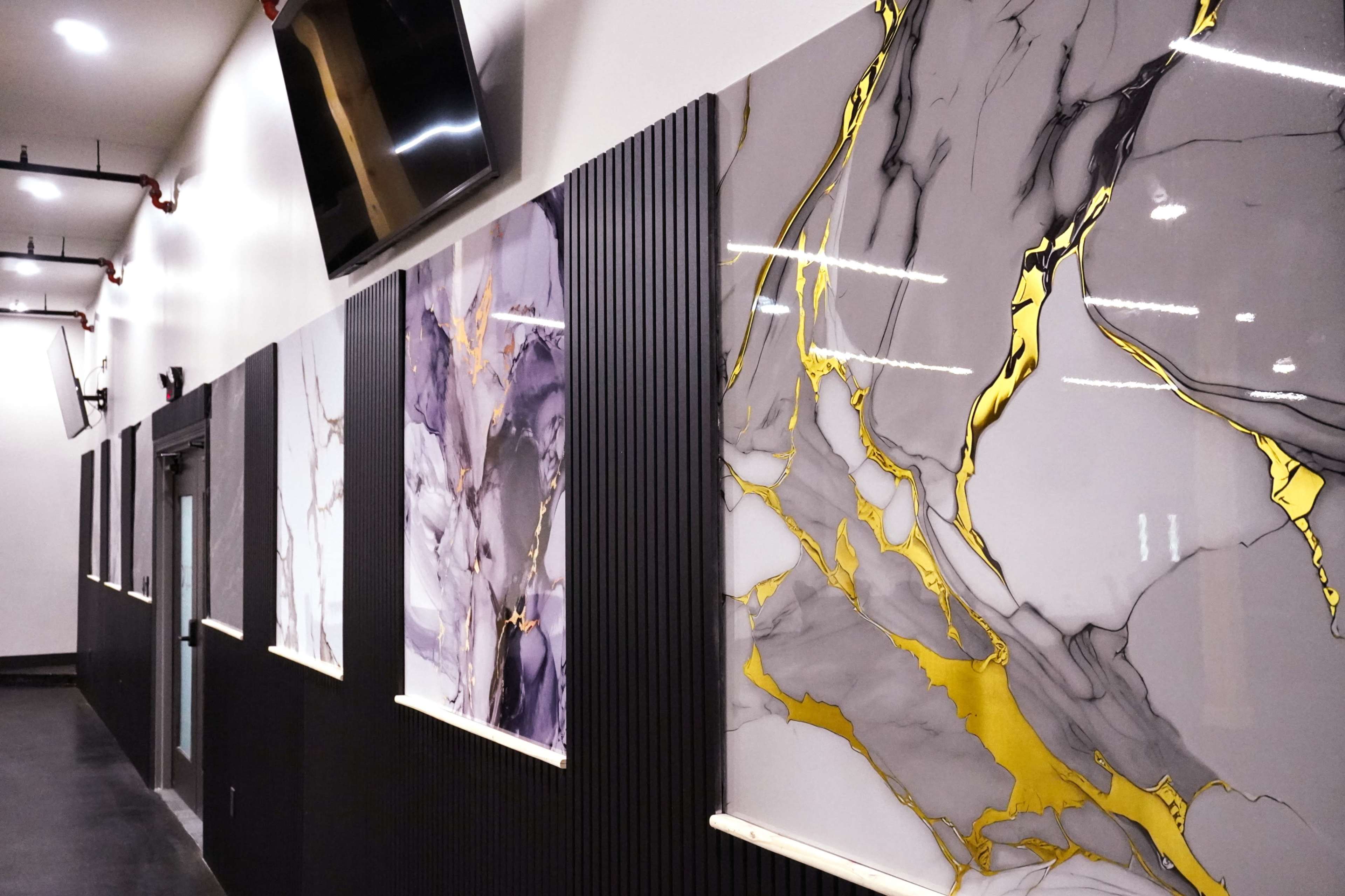 The image shows a hallway with a series of large, decorative panels featuring abstract marble designs with gold accents mounted on a wall with black and white finishes.