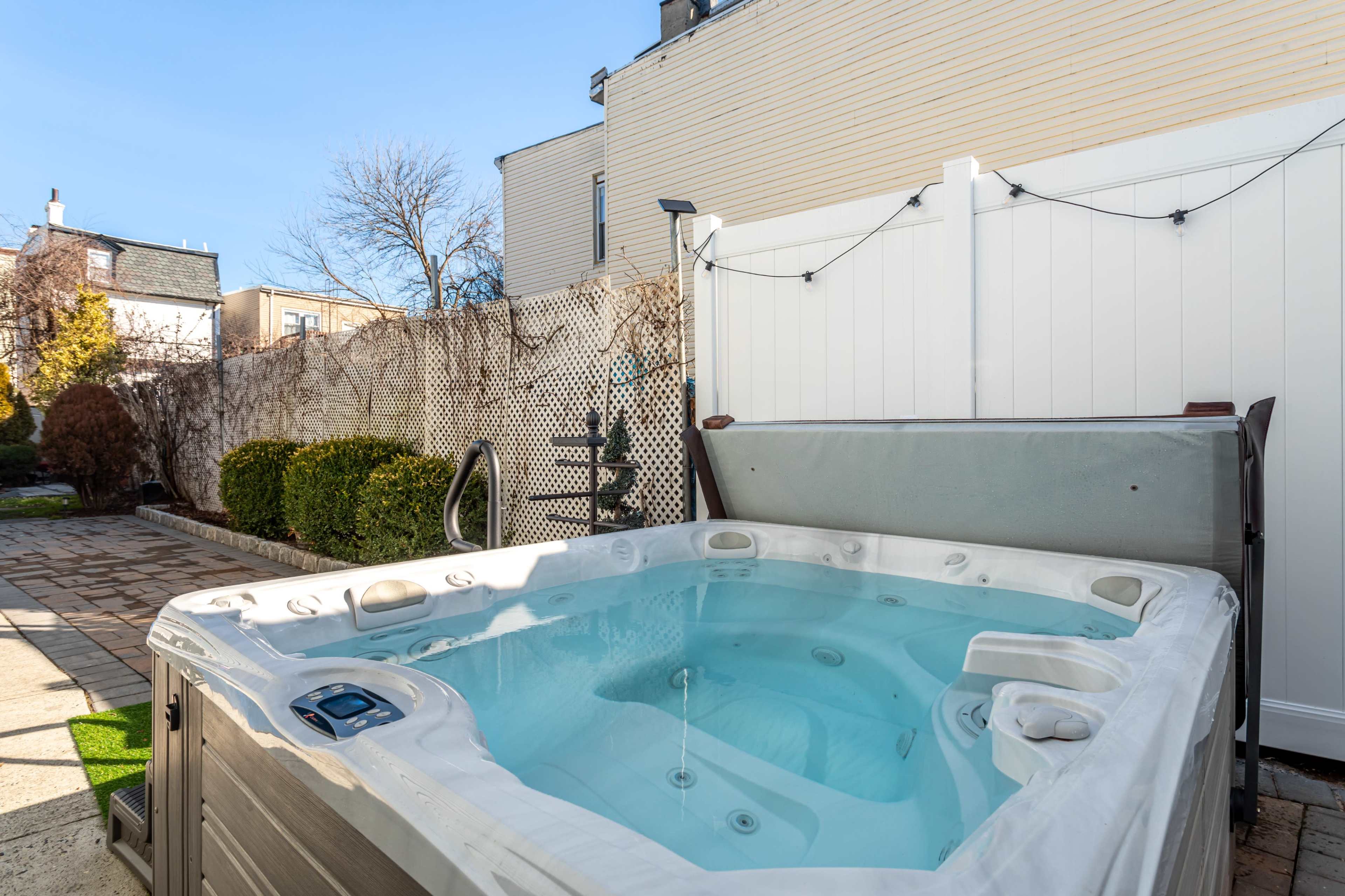 A hot tub bordered by a white fence and a landscaped garden in a residential setting.
