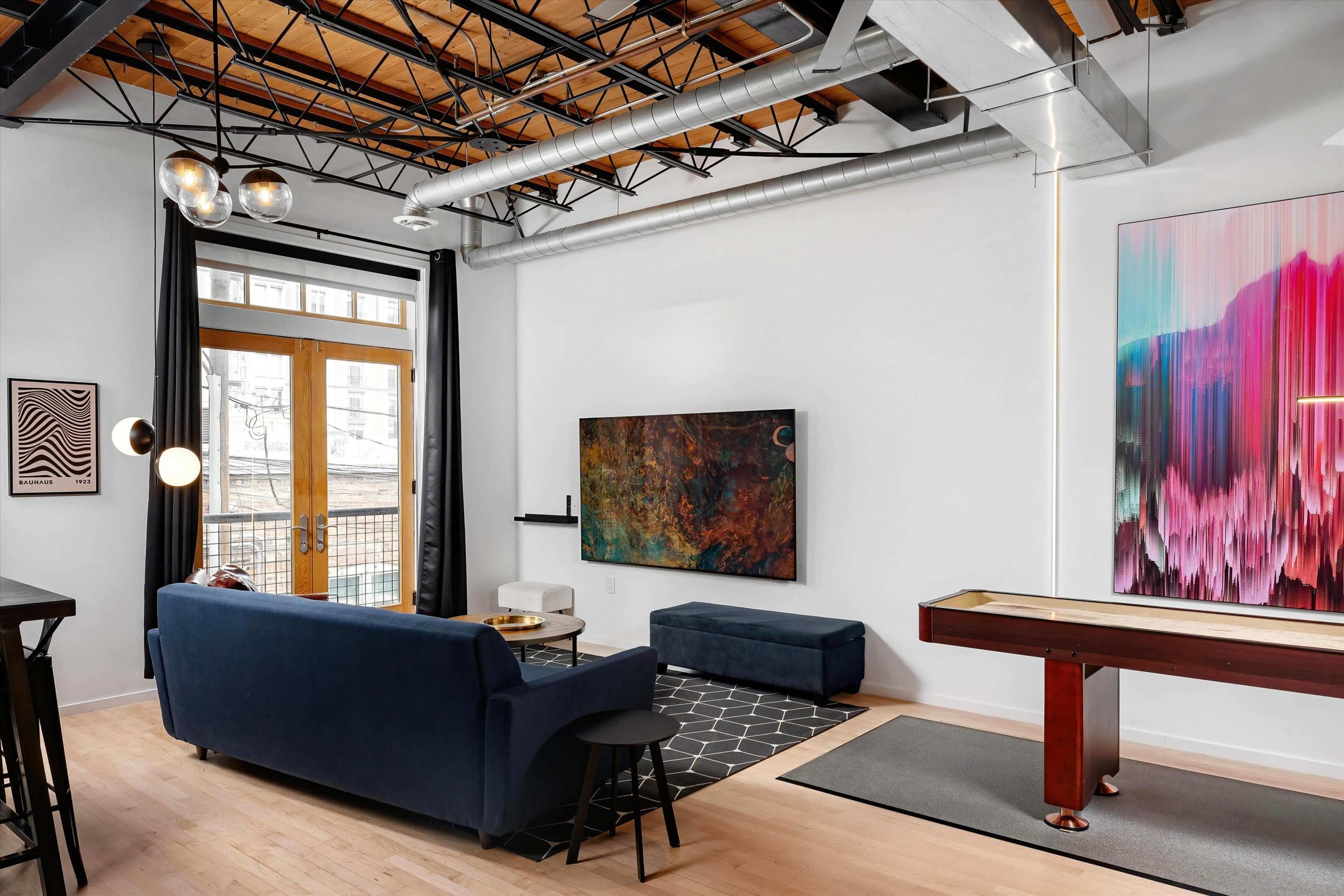 The image shows a modern living room featuring a blue couch, a wall-mounted television, a coffee table, and a colorful abstract artwork.