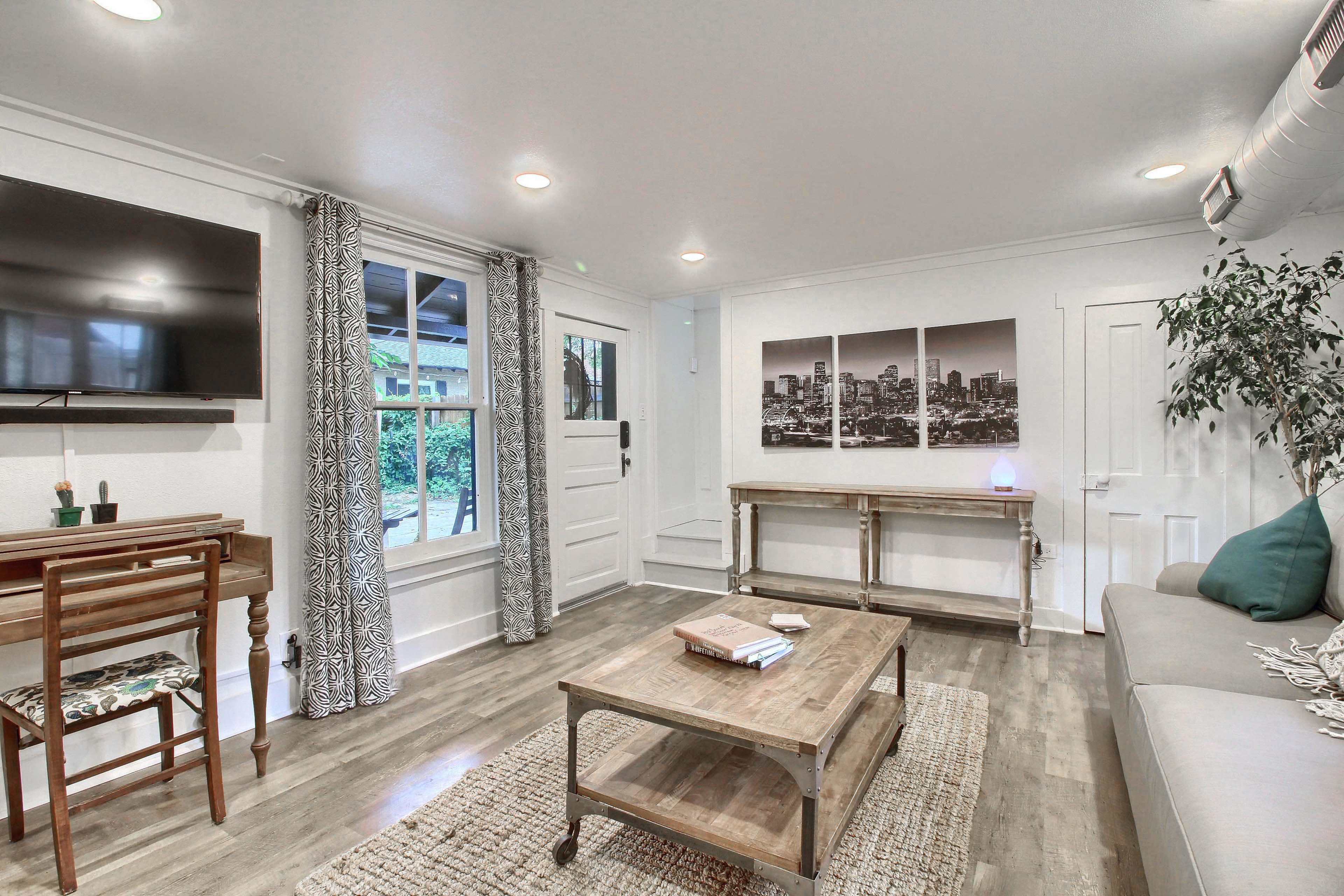 A modern living room with a television, a small wooden table, a couch, and large windows letting in natural light.