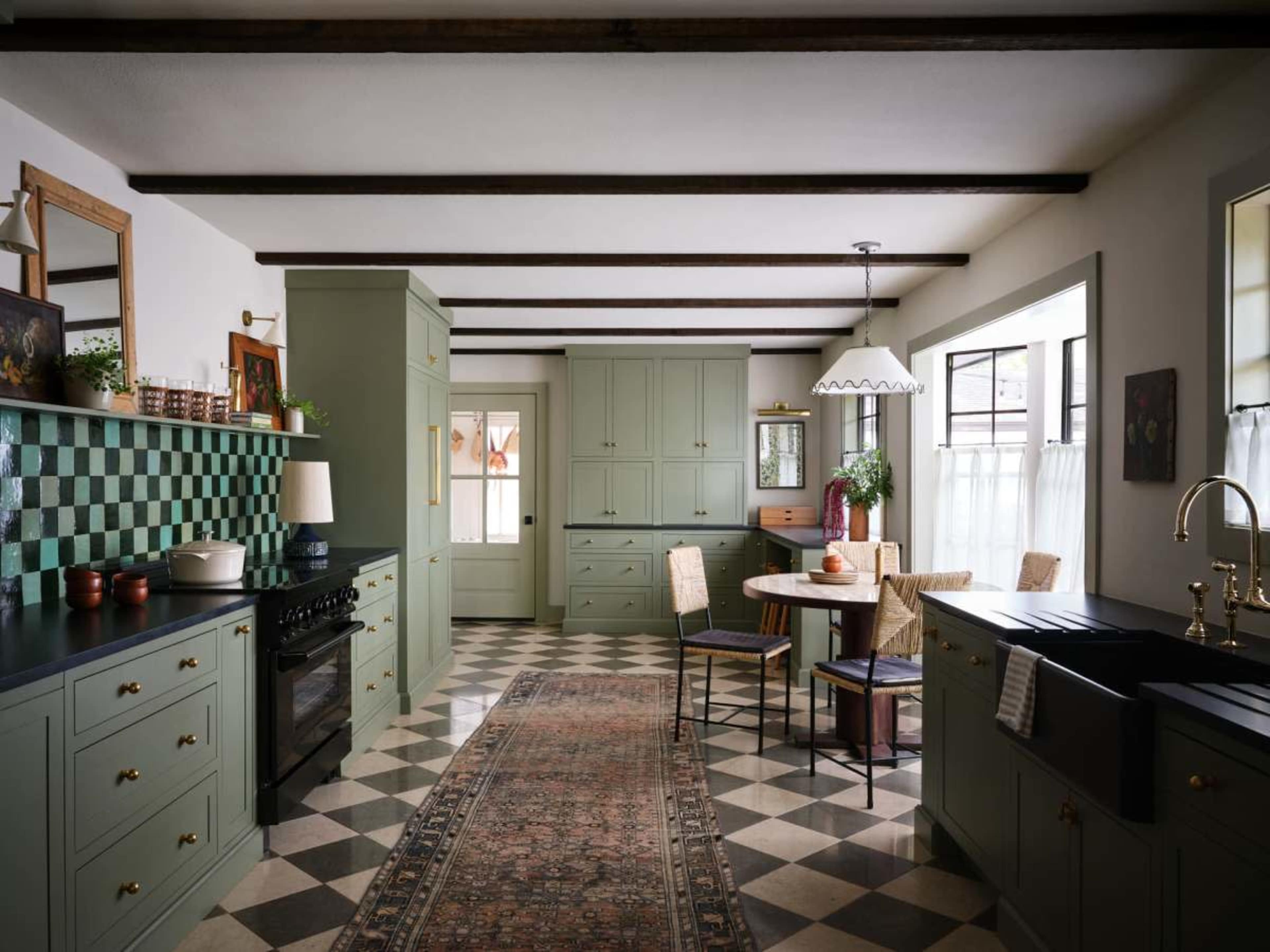 The image shows a modern kitchen featuring green cabinetry, a circular dining table, and a patterned floor with black and white tiles.