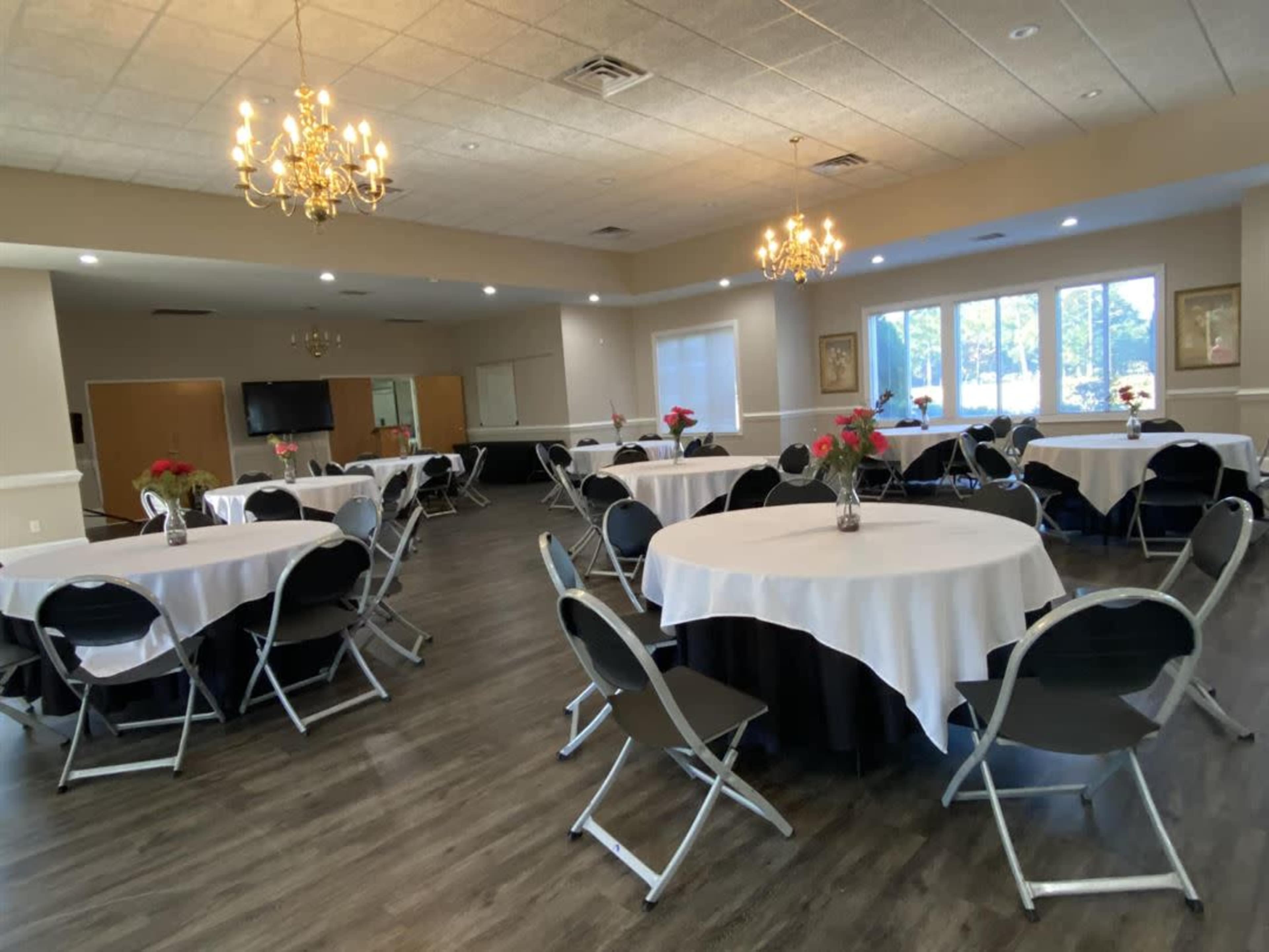 A banquet hall set up with circular tables covered in white tablecloths and chairs arranged around them, with chandeliers hanging from the ceiling.