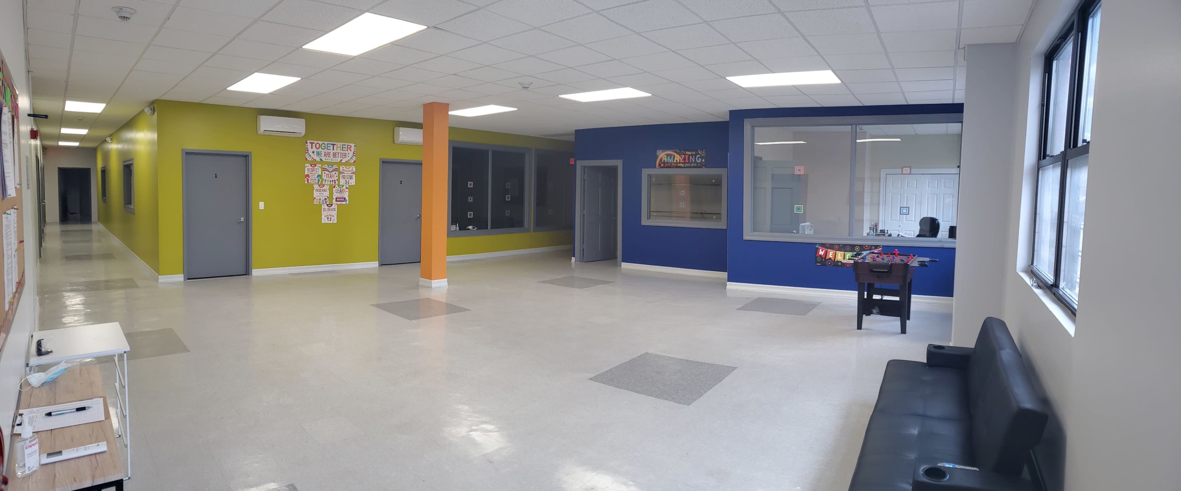 The image shows a brightly lit hallway with green and blue walls, doorways on either side, and a black sofa against one wall.