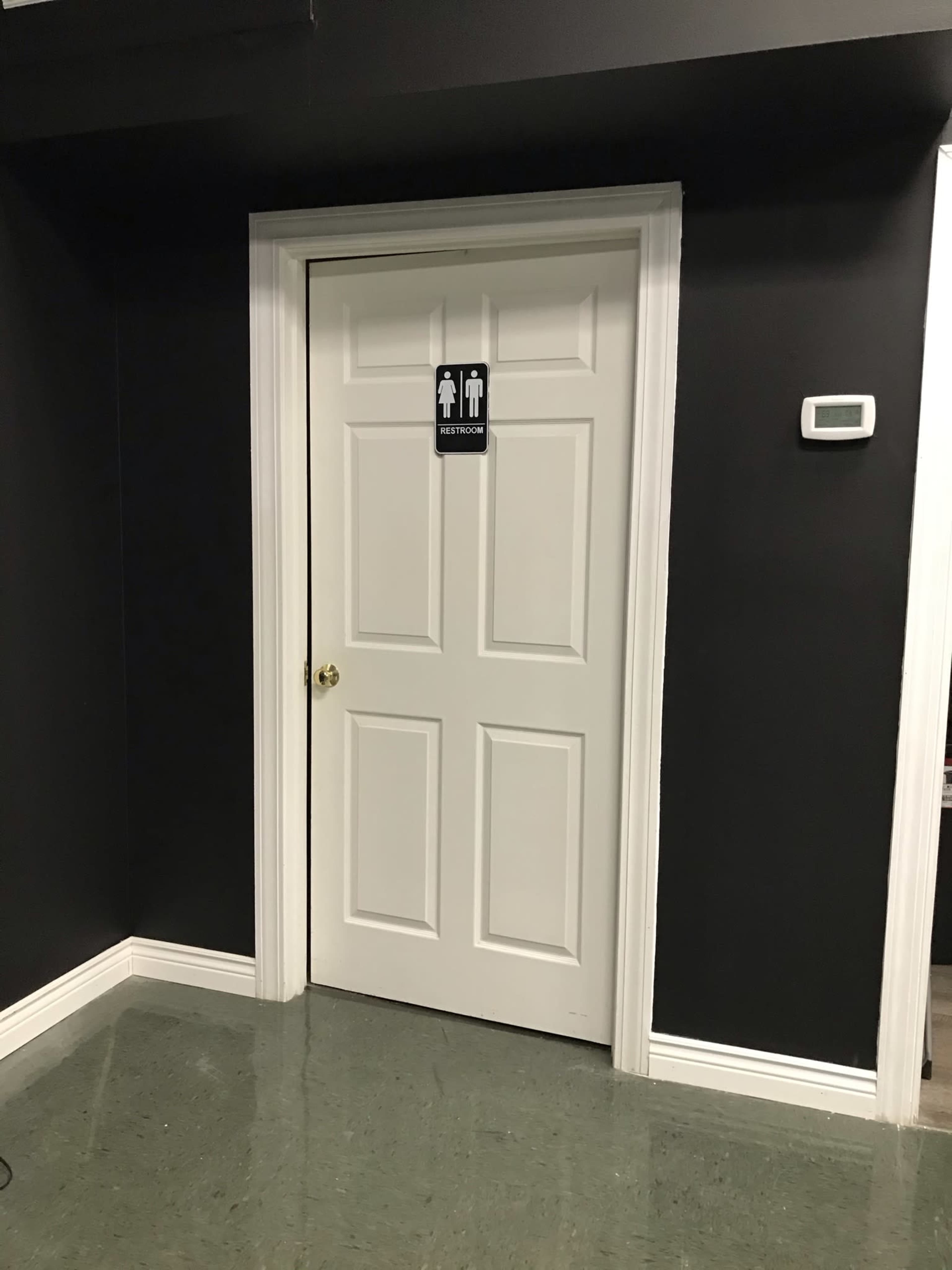 A white door labeled "RESTROOM" is set into a black wall, with a thermostat mounted nearby.