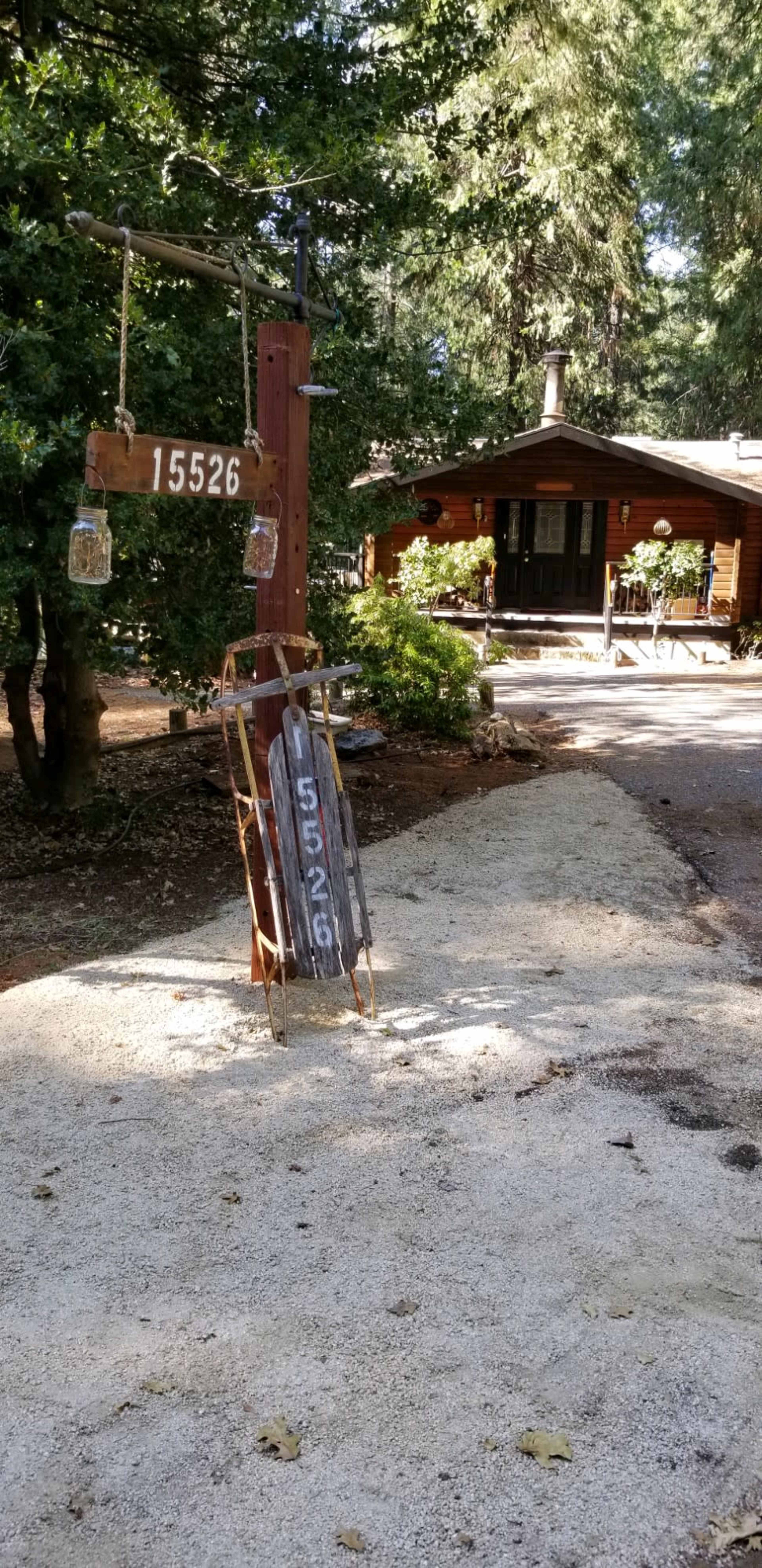 A rustic house with a wooden sign displaying the number 15526, set along a gravel driveway surrounded by trees.