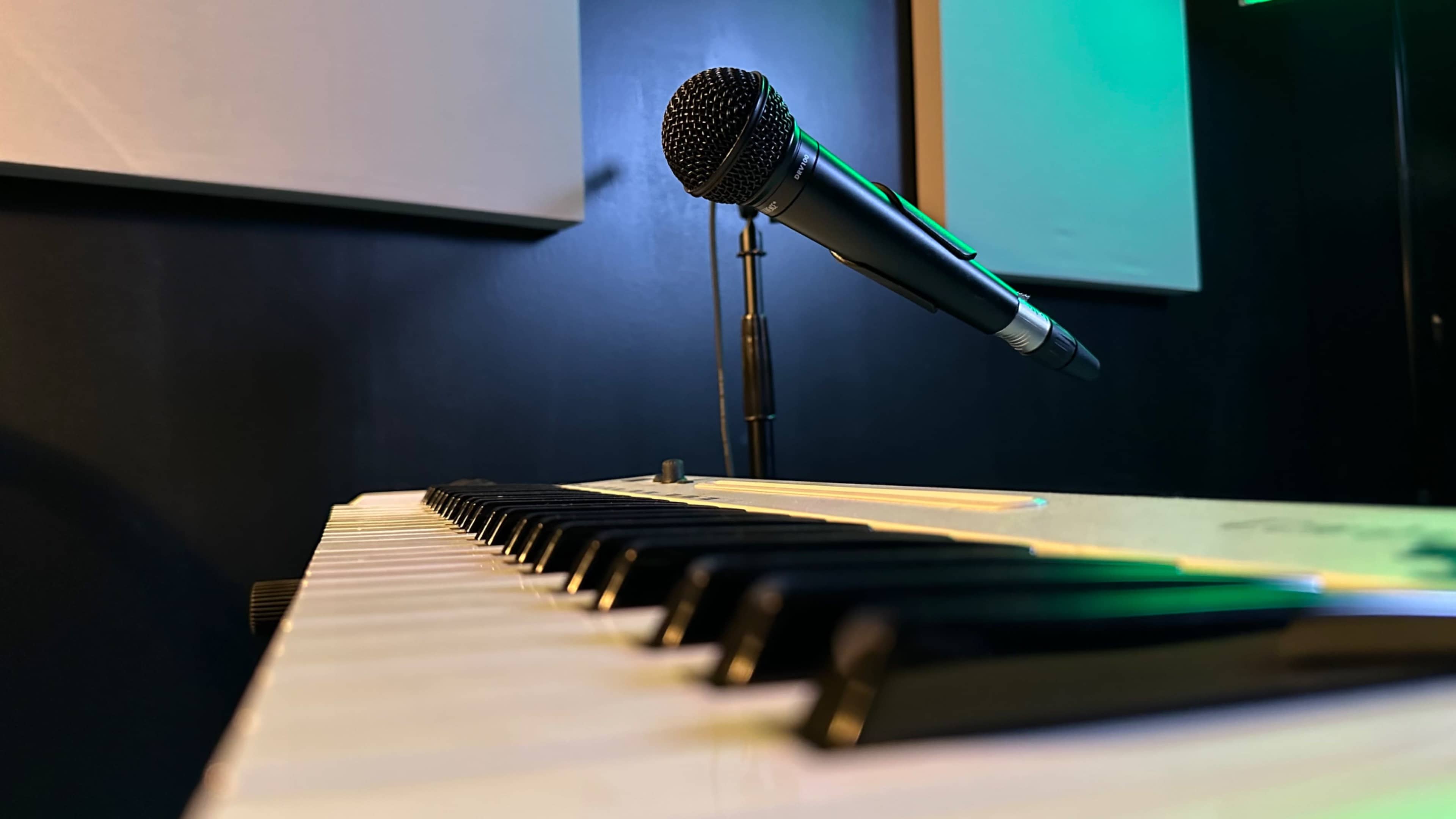 A microphone stands above a row of piano keys in a dimly lit music studio.