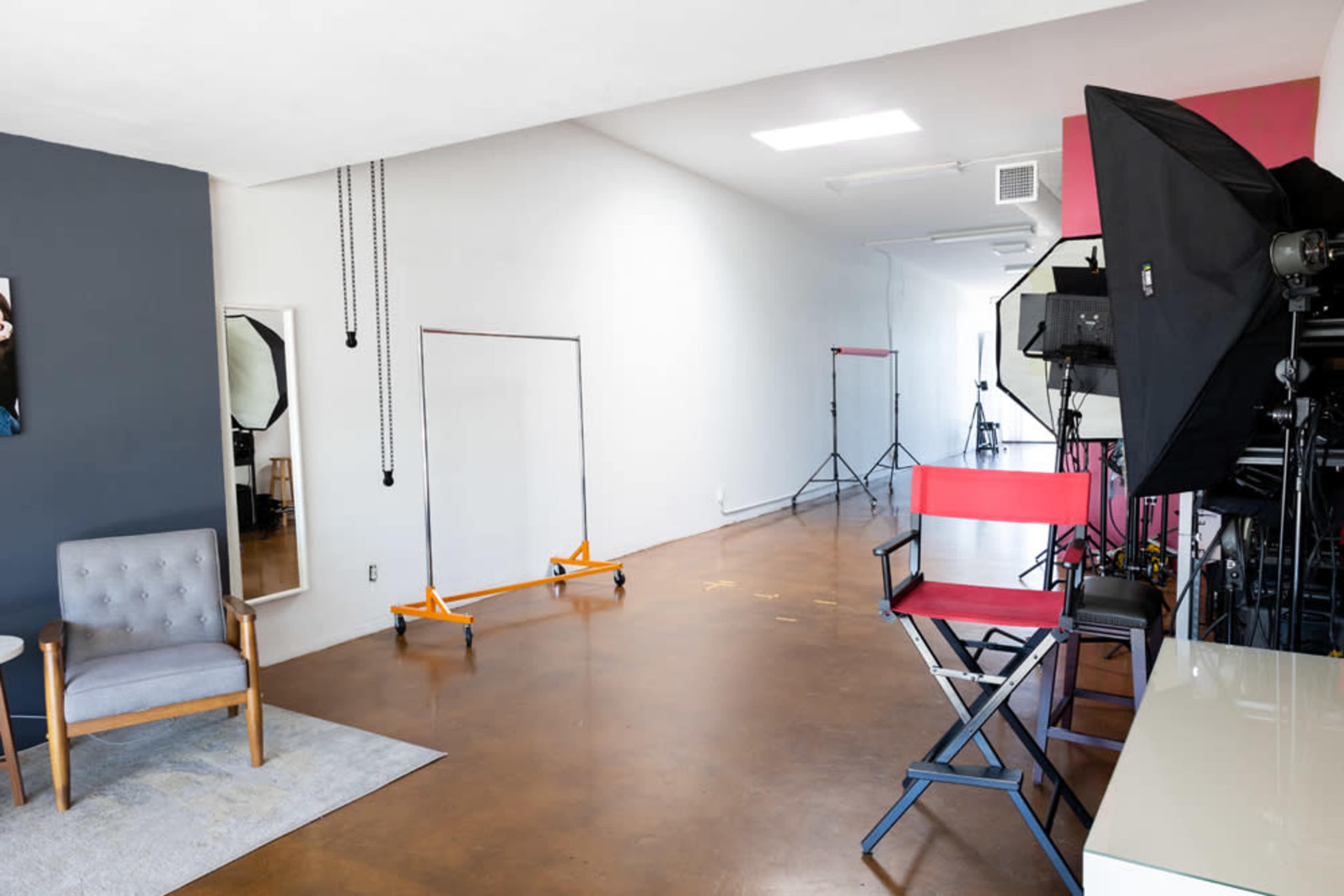 A spacious studio with a gray wall, a large mirror, a director's chair, and professional lighting equipment set up for photography.