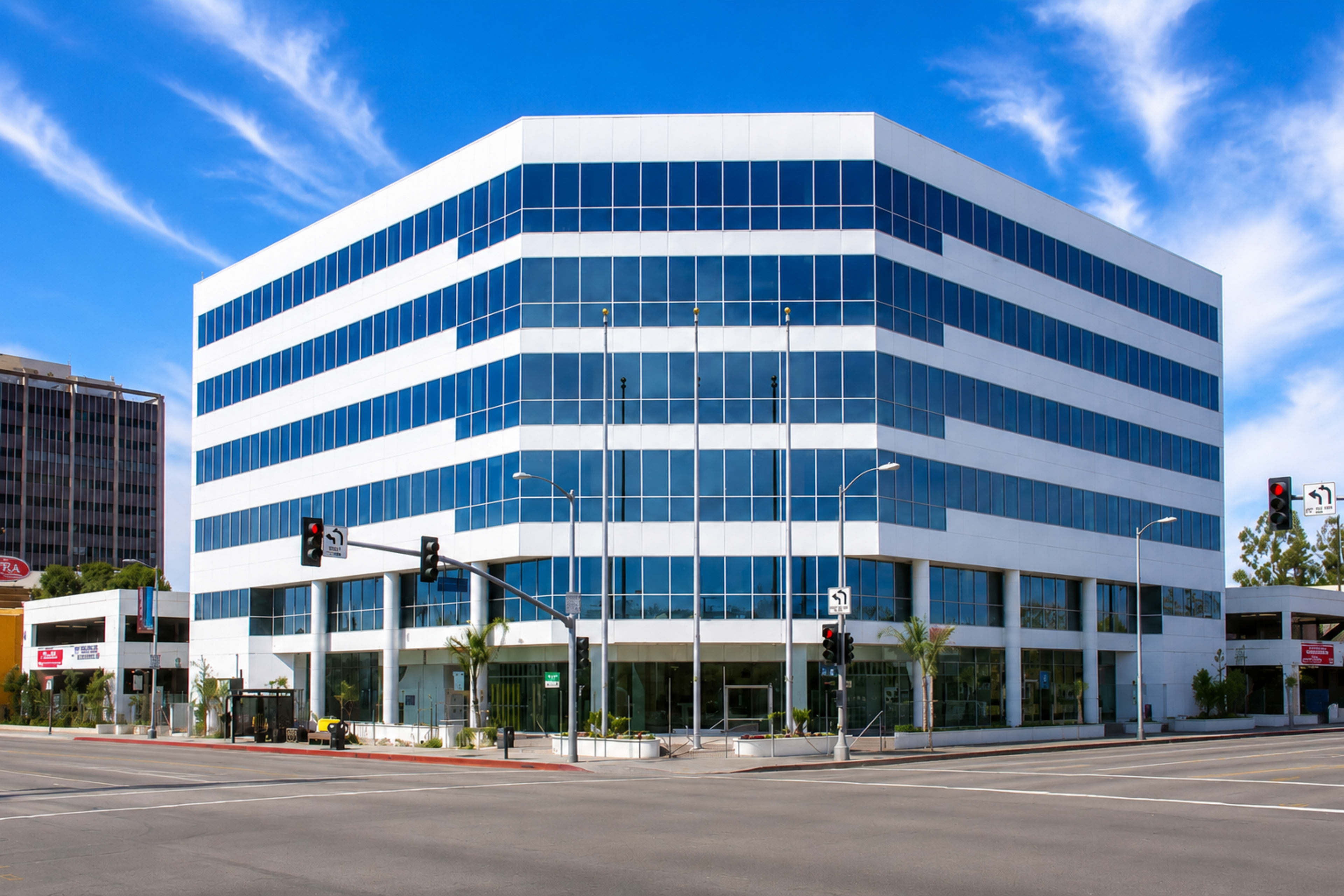 The image shows a modern glass-fronted office building at a street intersection with traffic signals.