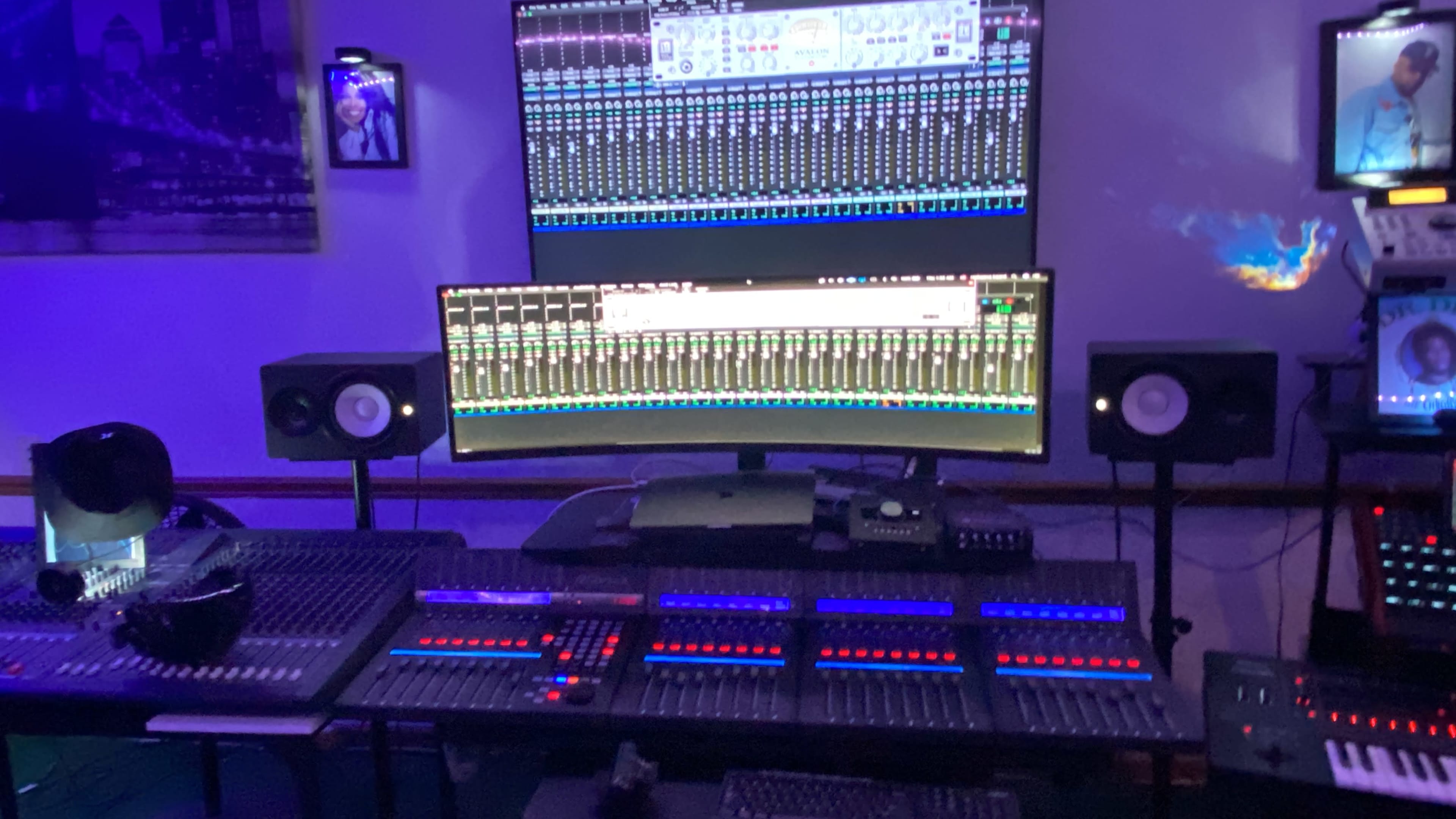 A music production studio with multiple large computer screens displaying audio mixing software, surrounded by speakers and a control panel with illuminated buttons.