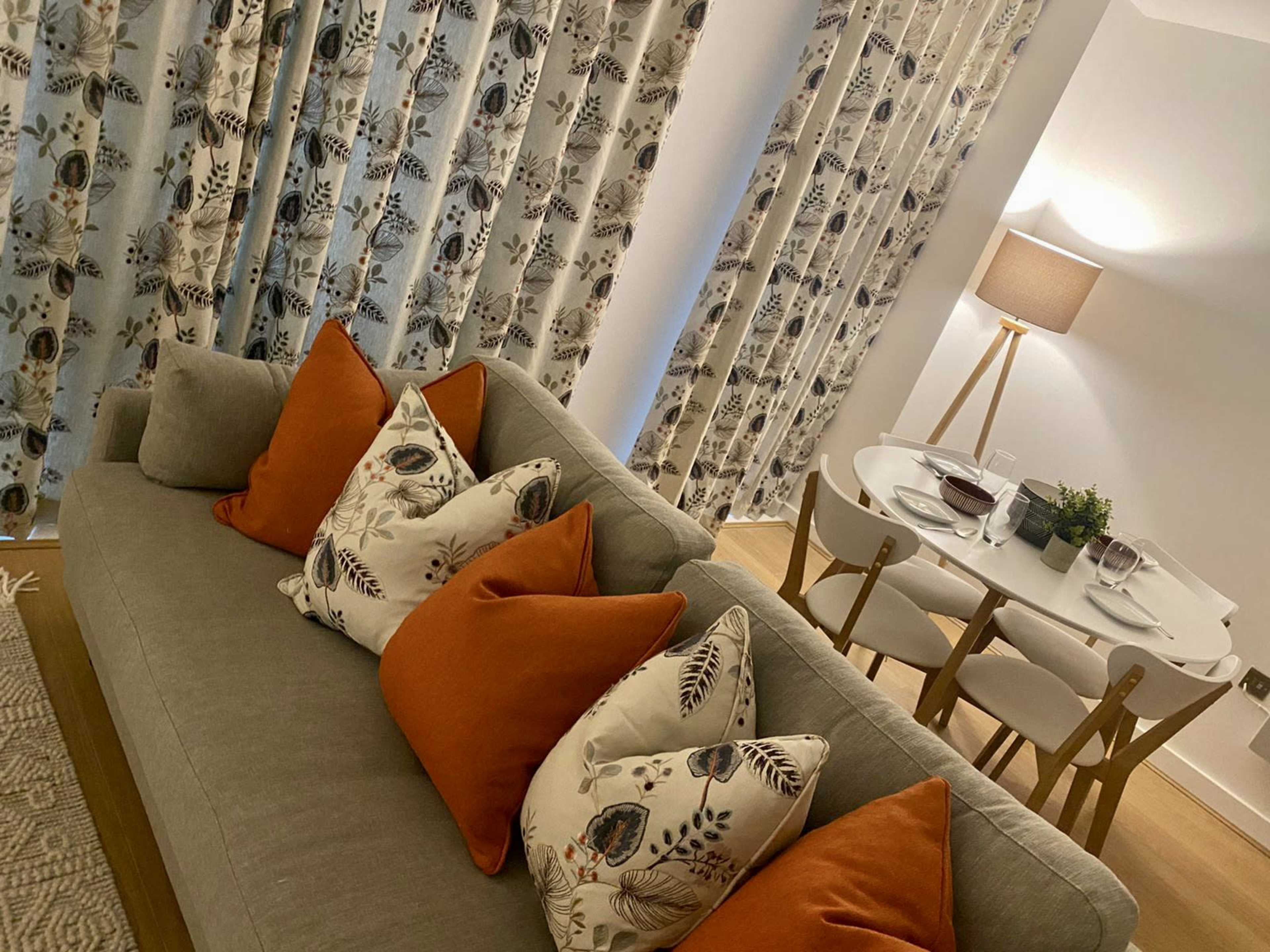 A modern living room featuring a sofa with decorative pillows, patterned curtains, and a dining area with a round table set for two.