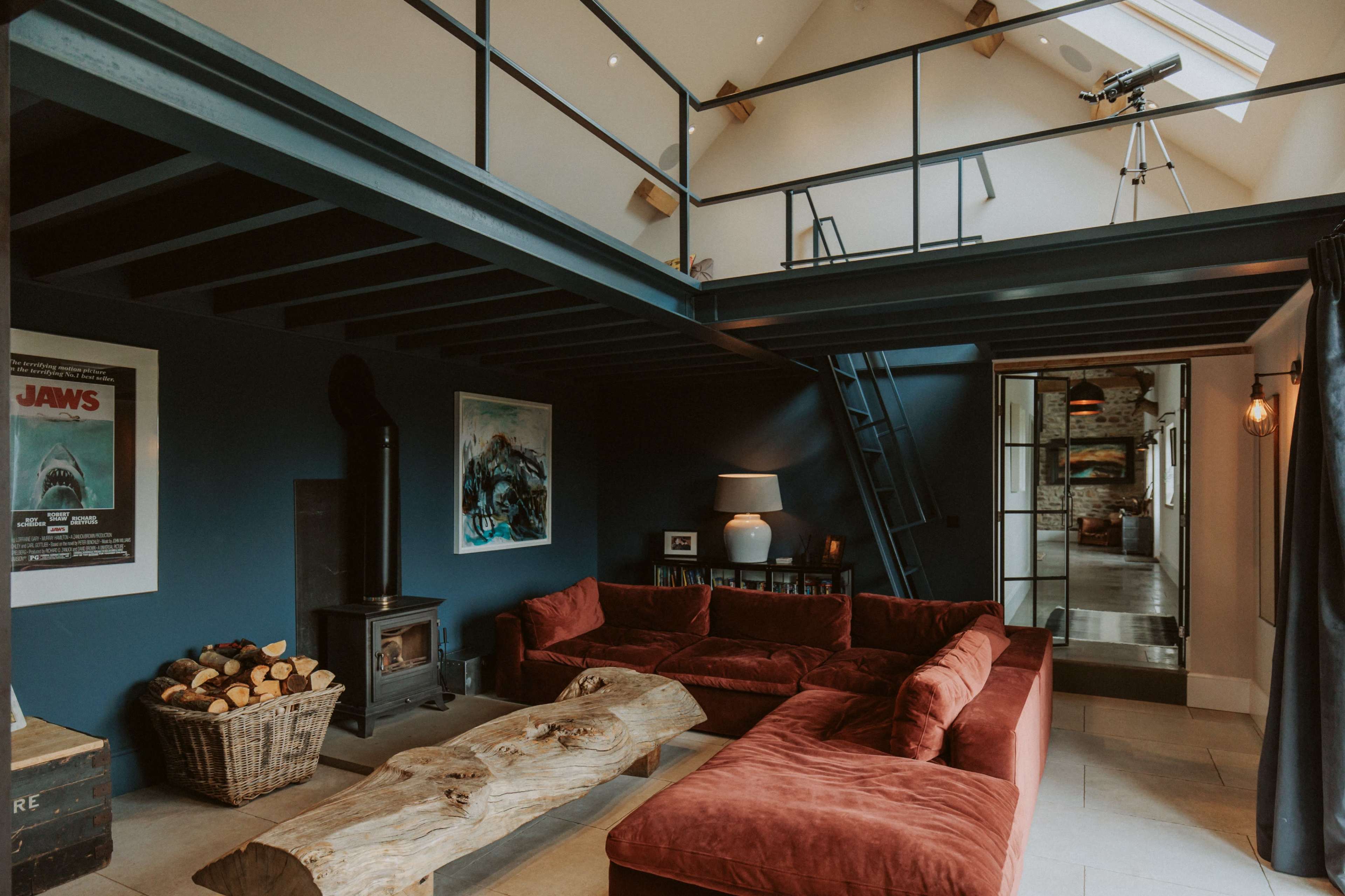 A modern living room featuring a red sectional sofa, a wooden coffee table, a wood-burning stove, and a staircase leading to a loft area with a telescope.
