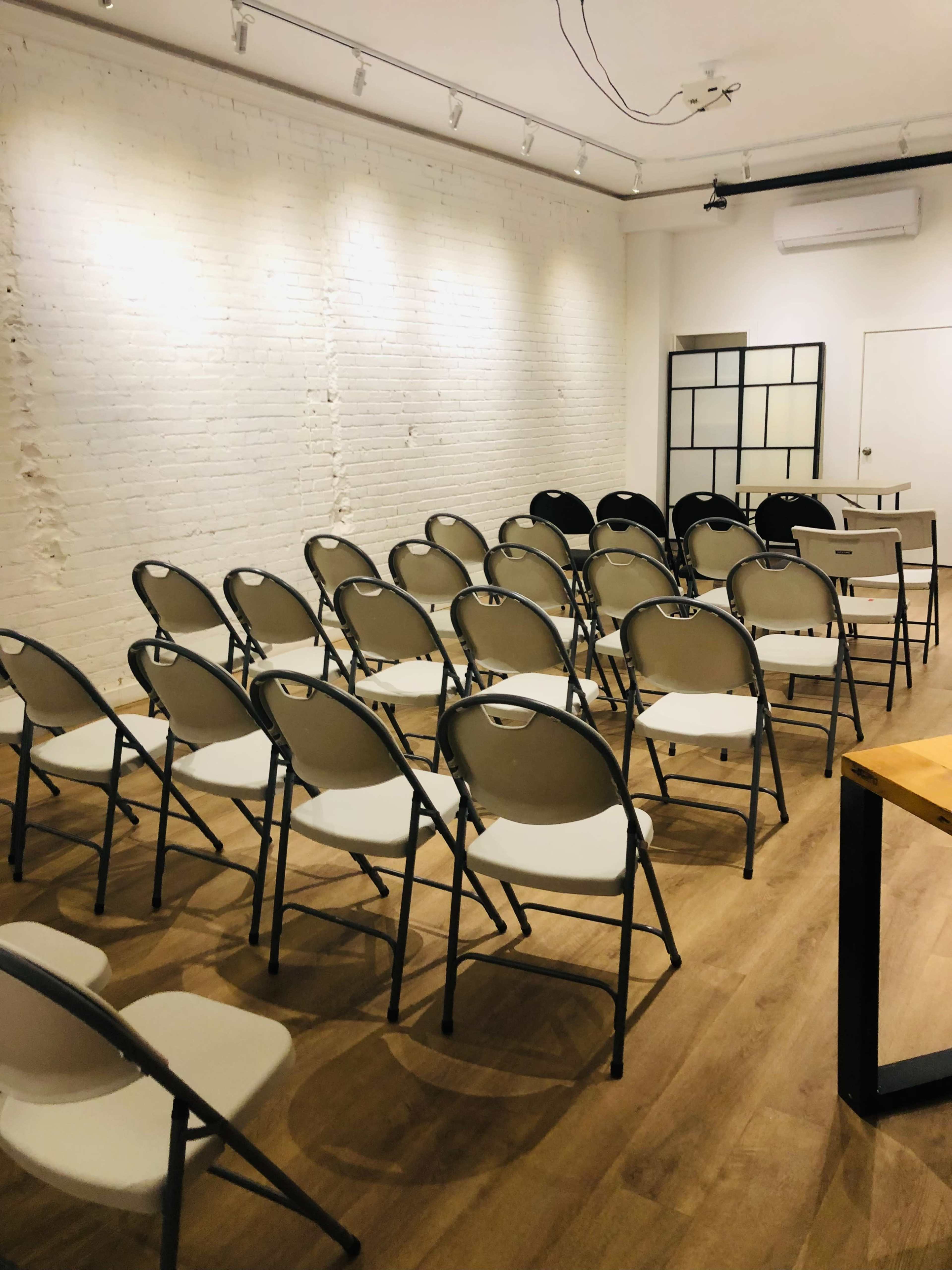 A room with white brick walls and a row of neatly arranged folding chairs facing a blank wall.