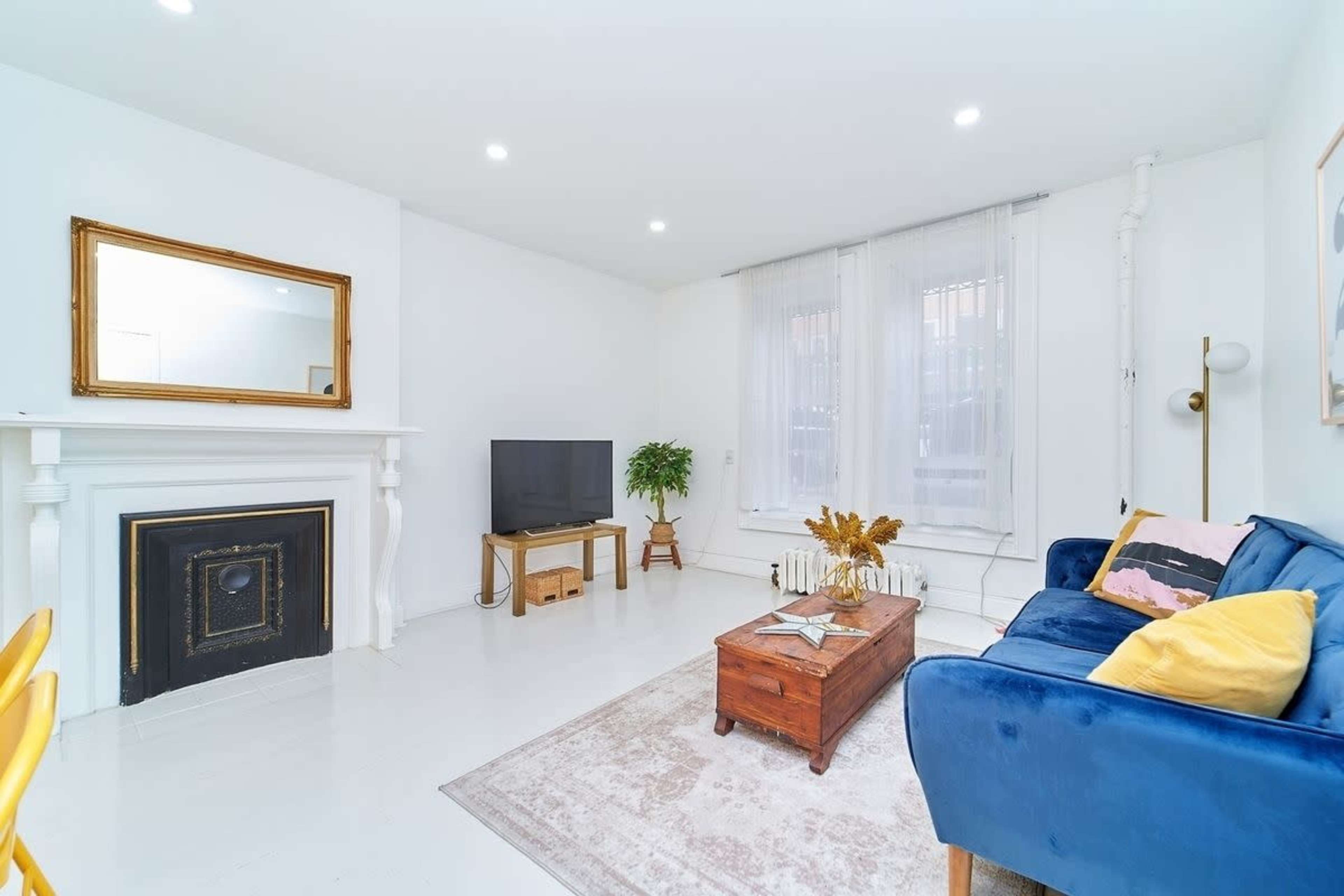The living room features a blue sofa, a wooden coffee table, a television, and a decorative fireplace against a white backdrop.