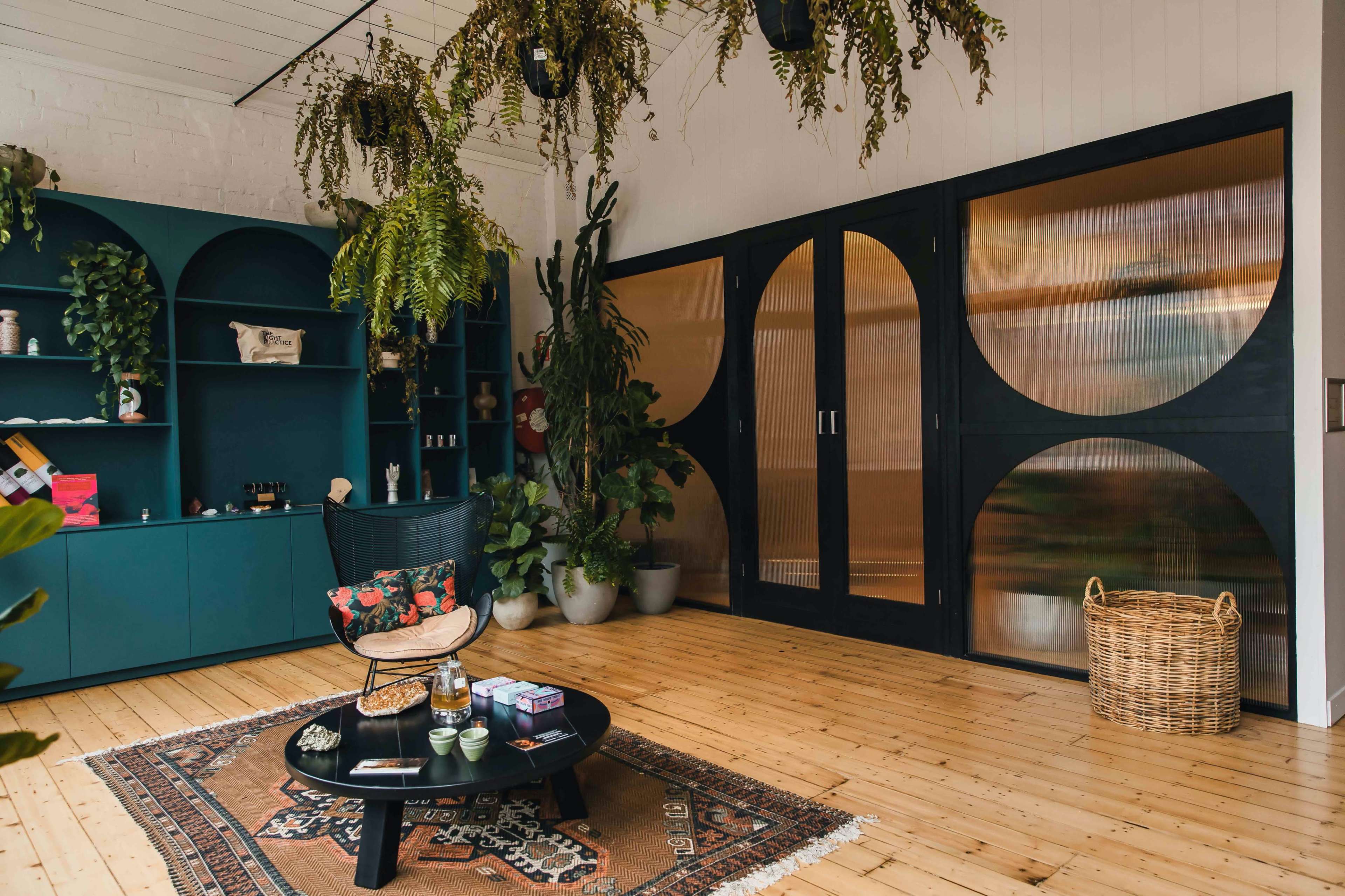 A modern interior features a wooden floor, a green shelving unit, a round coffee table, potted plants, and sliding doors with opaque panels.