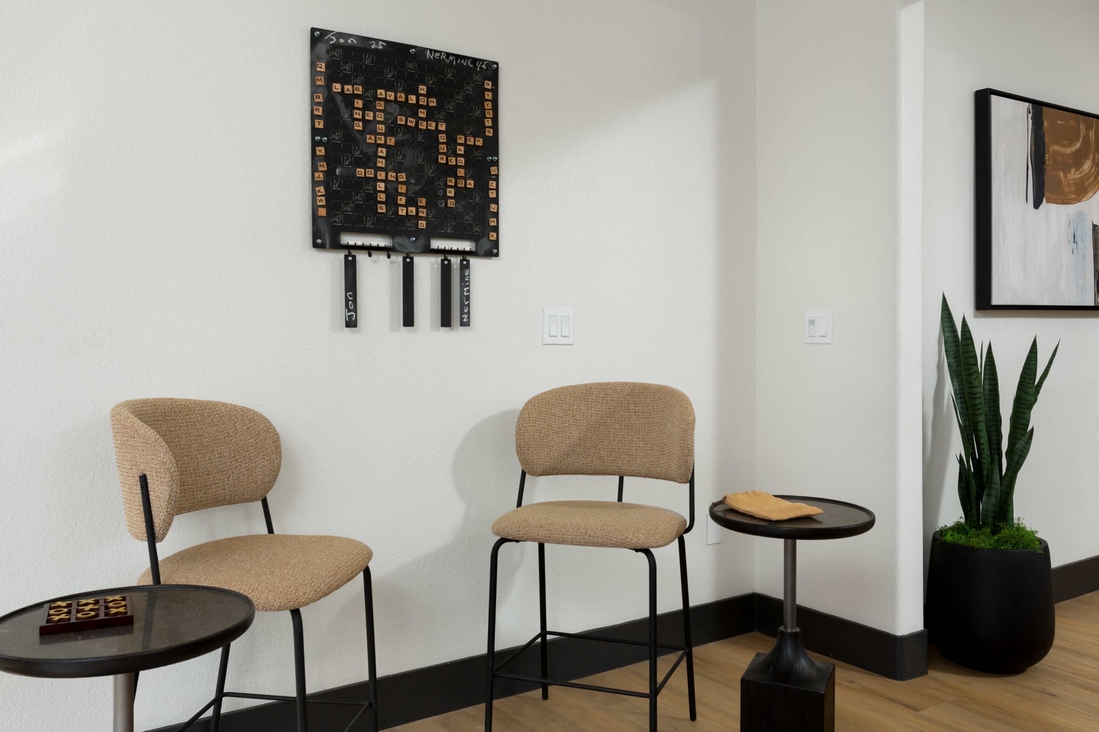 Two modern upholstered stools next to small tables, with a wall-mounted board featuring a grid of letters and numbers above them.