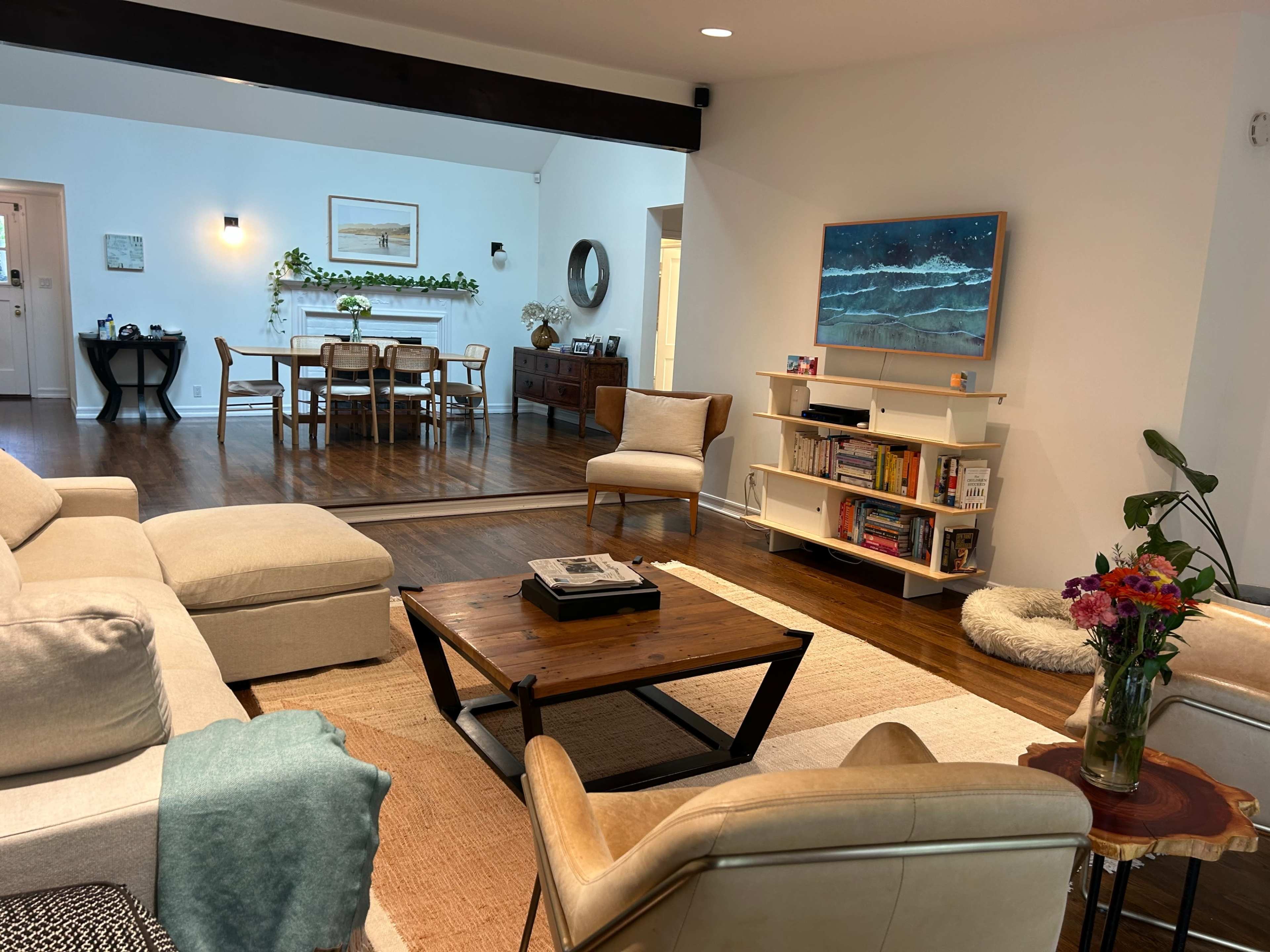 The image shows a modern living room with a large sofa, a coffee table, a bookshelf, and a dining area in the background.