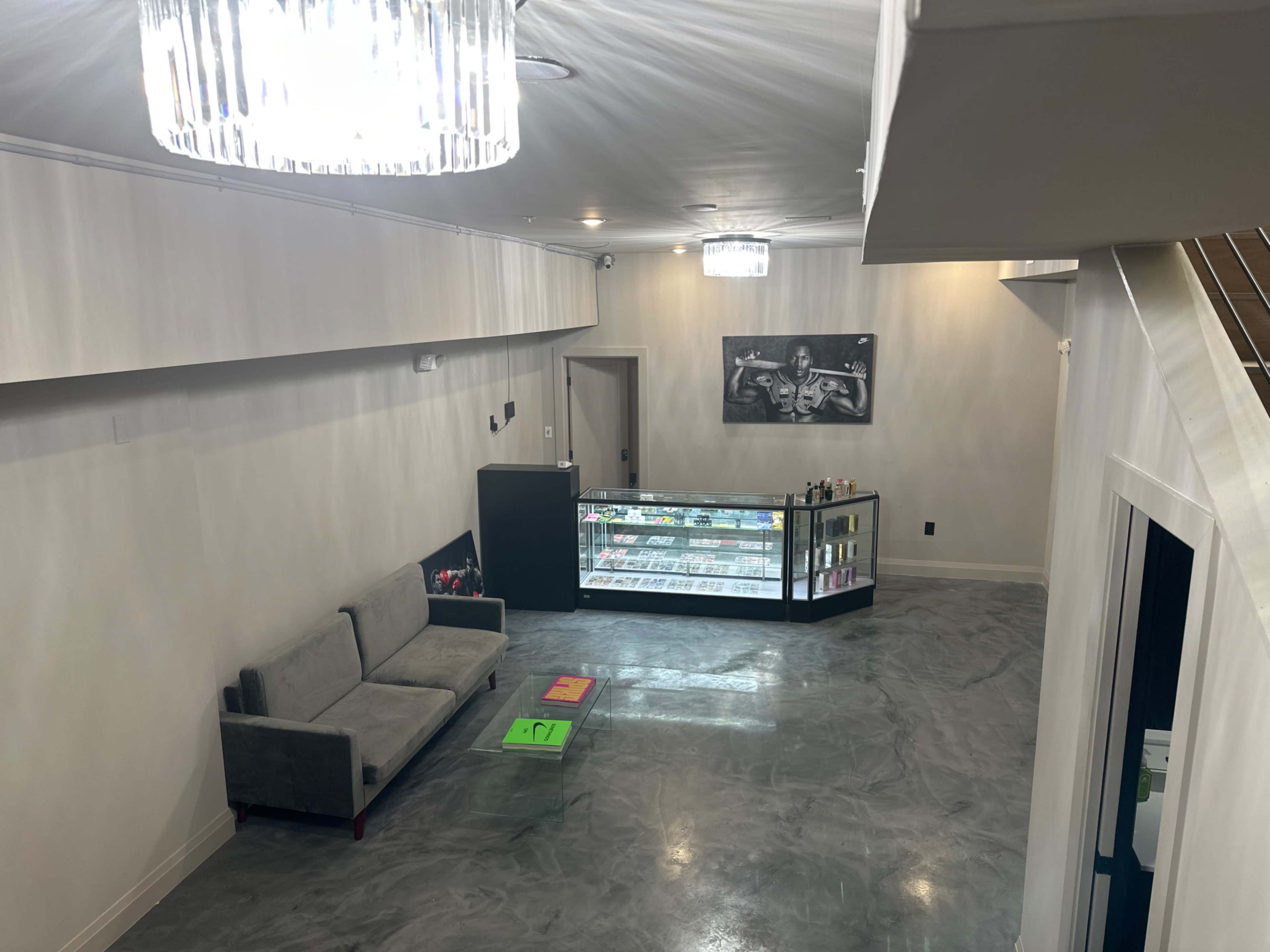 A spacious interior of a modern retail space featuring a gray sofa, an illuminated display case, and artistic wall decor under a chandelier.