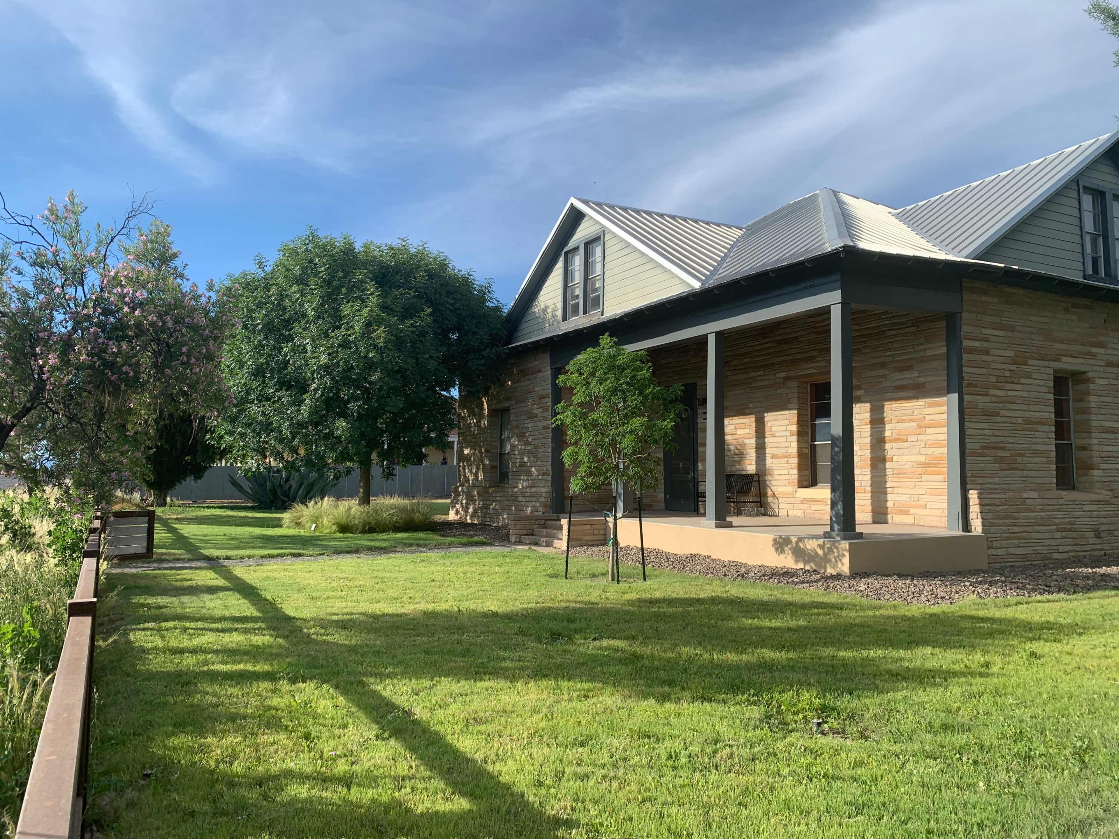 A stone and wood house with a metal roof is surrounded by a grassy yard and trees.