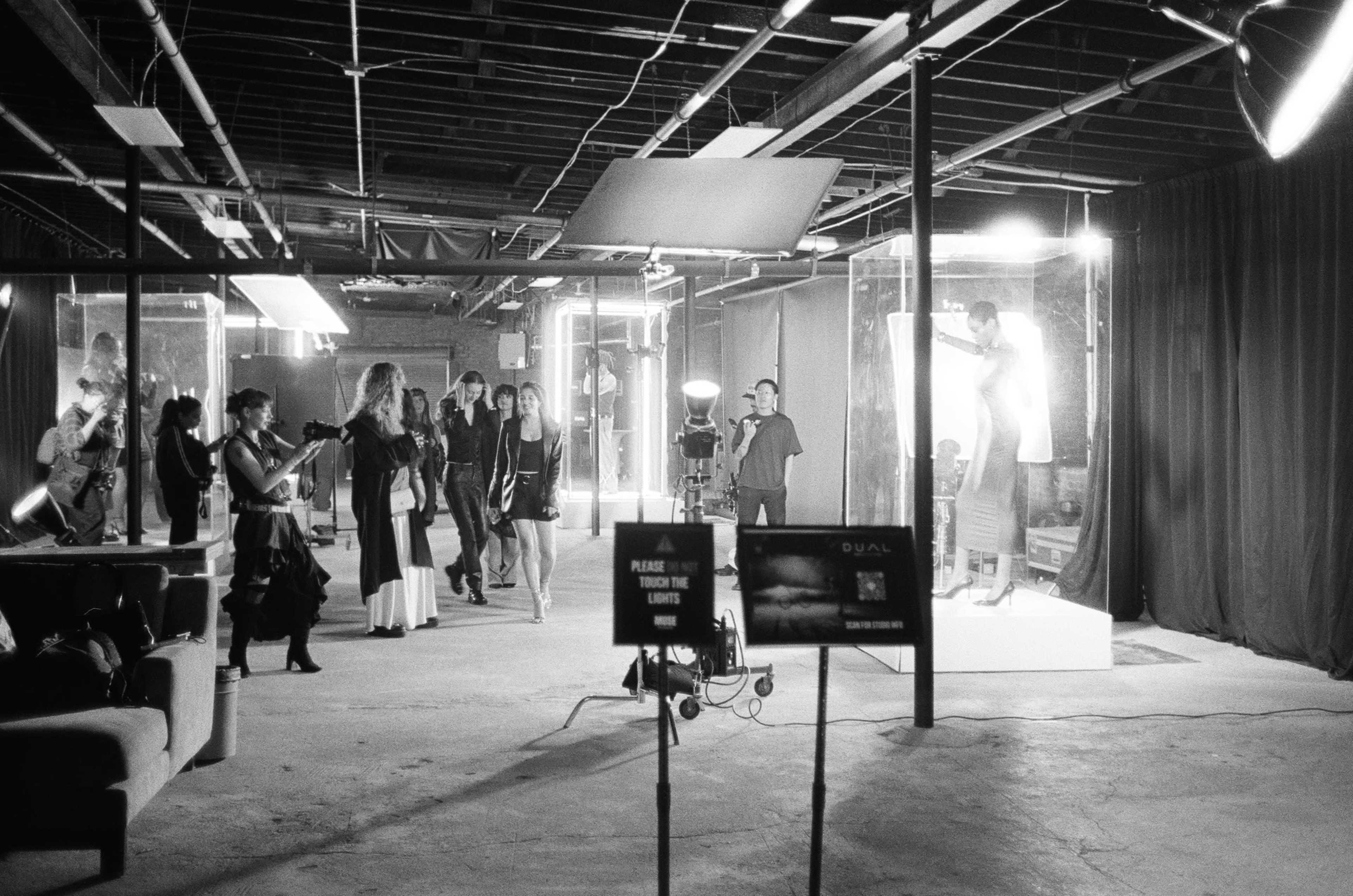 The scene depicts a dimly lit studio space with models and photographers, surrounded by glass display cases and studio lighting equipment.