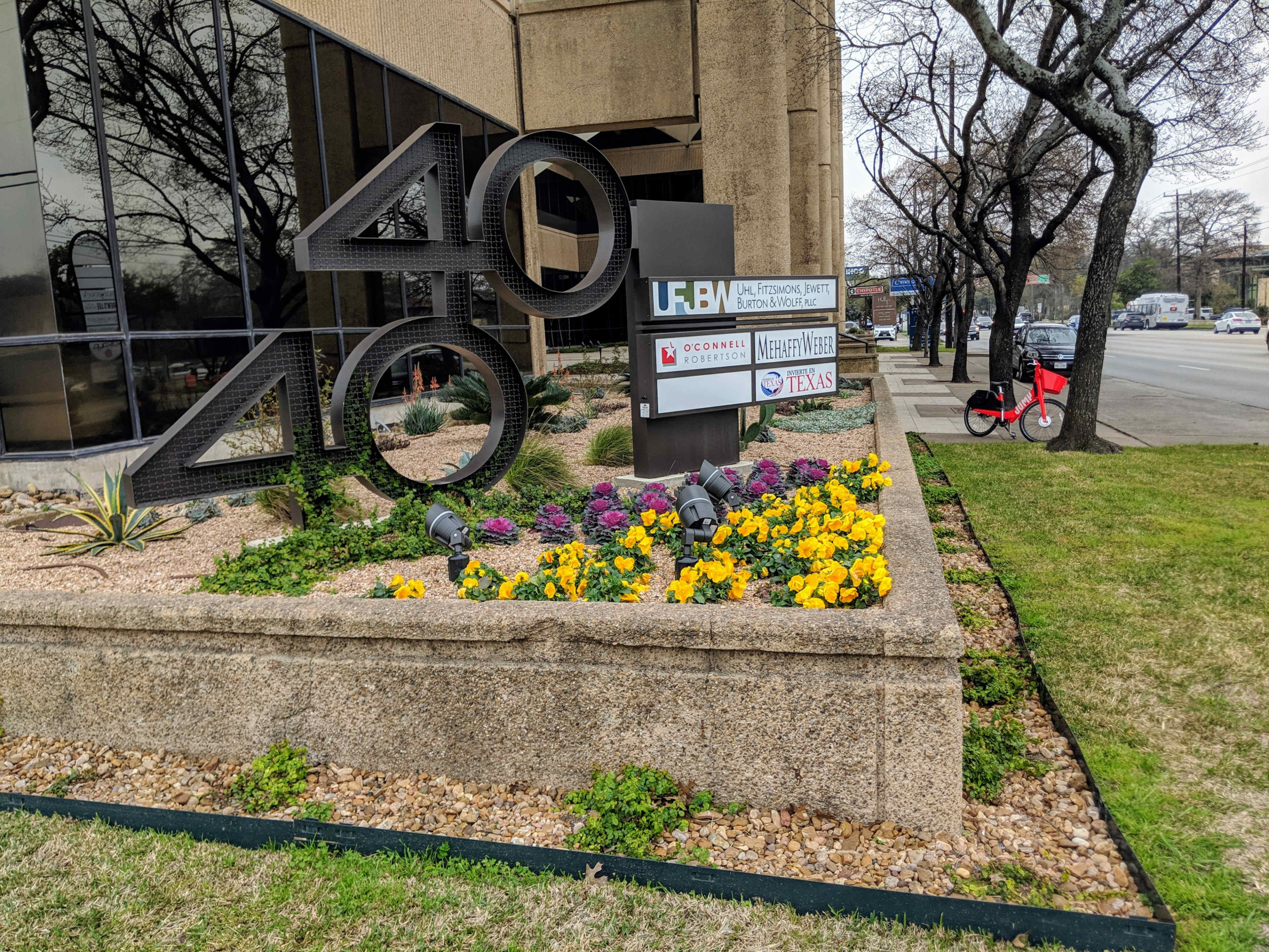 A landscaped area in front of a building featuring a large "4040" sign, colorful flowers, and business signage.