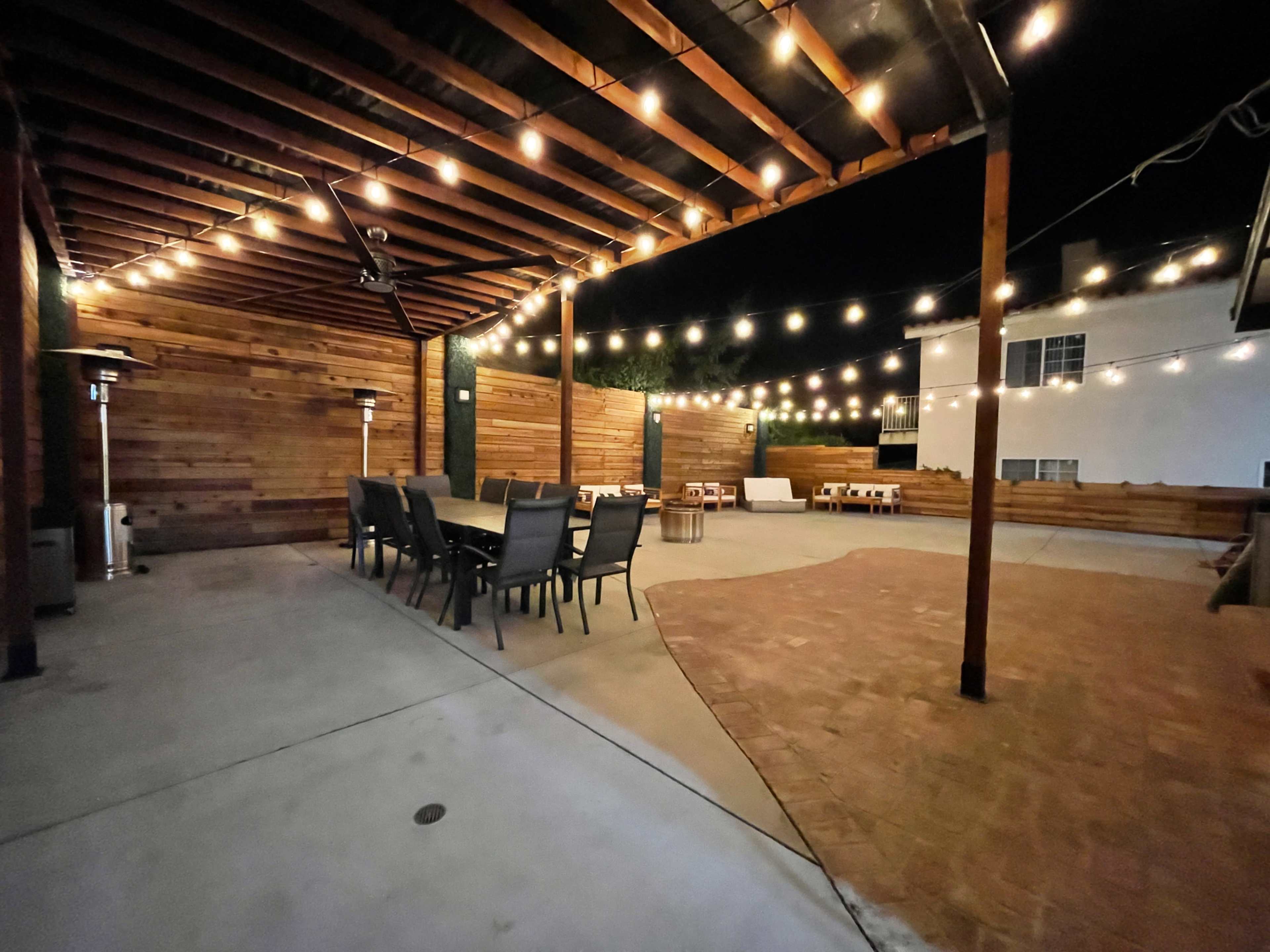 A spacious outdoor patio area at night, featuring wooden beams, string lights, and seating arrangements.