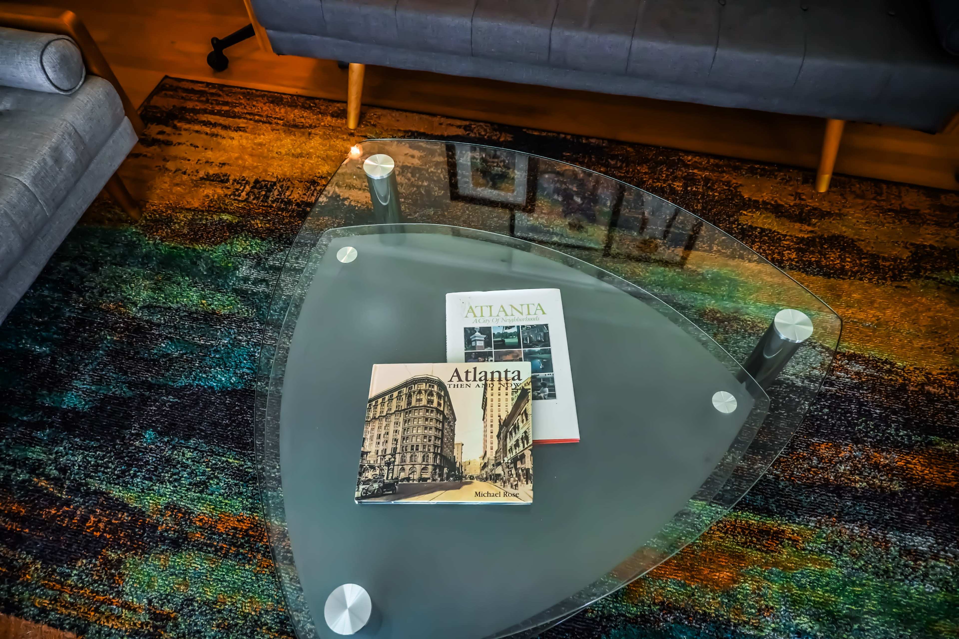A glass triangular coffee table sits on a colorful rug, with two books about Atlanta placed on top.