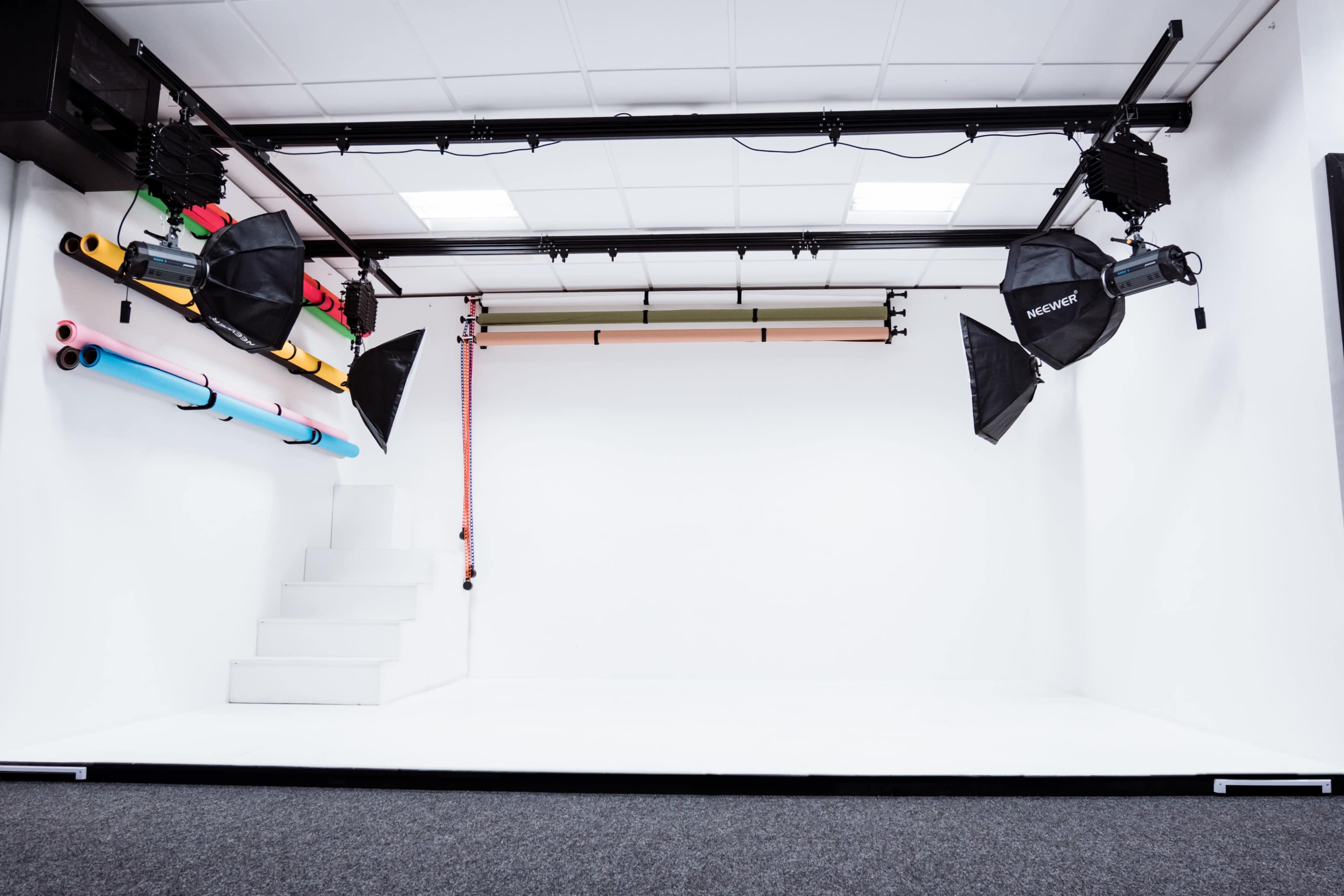 A photography studio with a white backdrop, lighting equipment, and colorful backdrops on the wall.