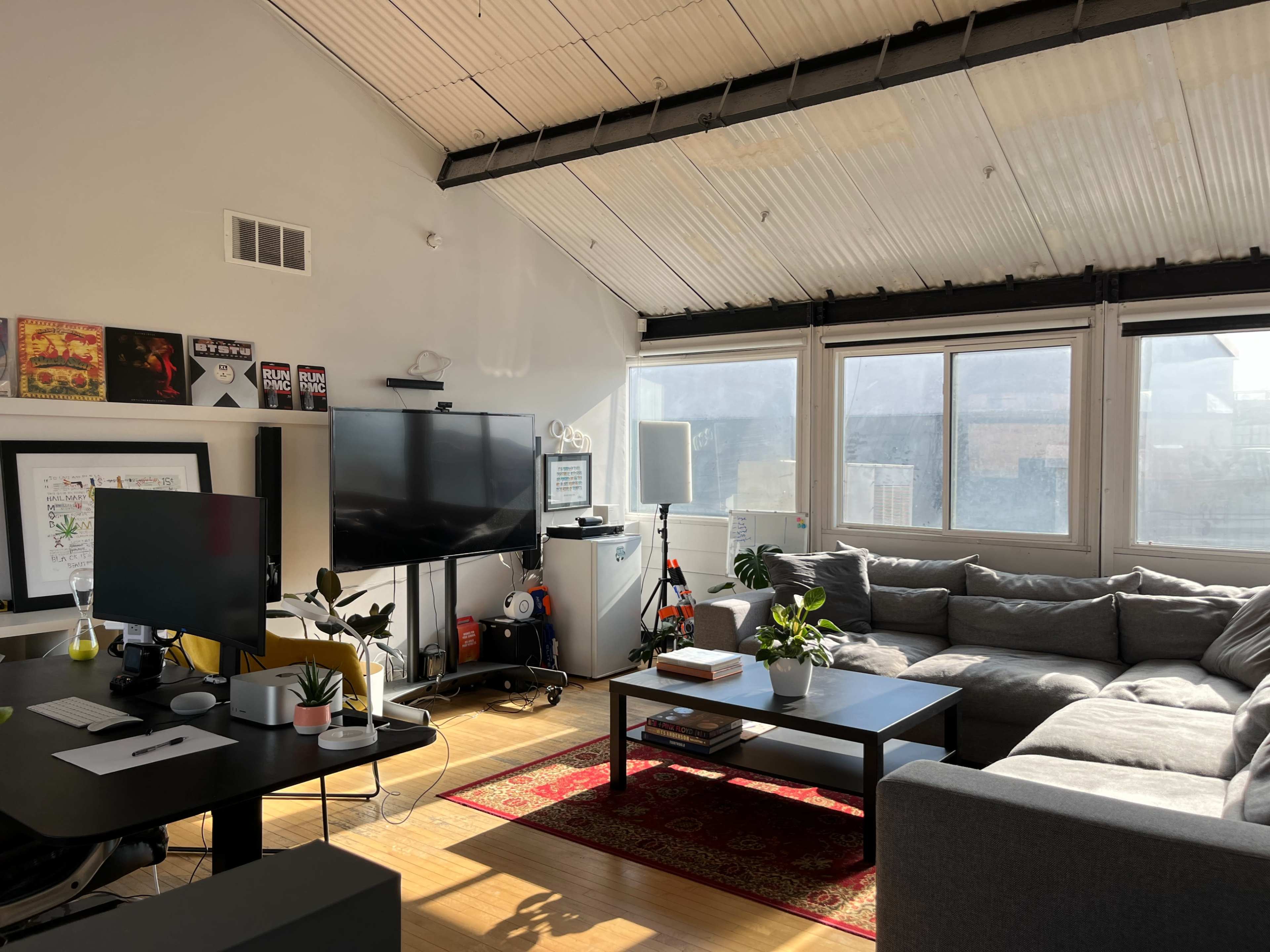 A bright living room with a large gray sectional sofa, a black coffee table, and a television on a stand, illuminated by natural light from large windows.