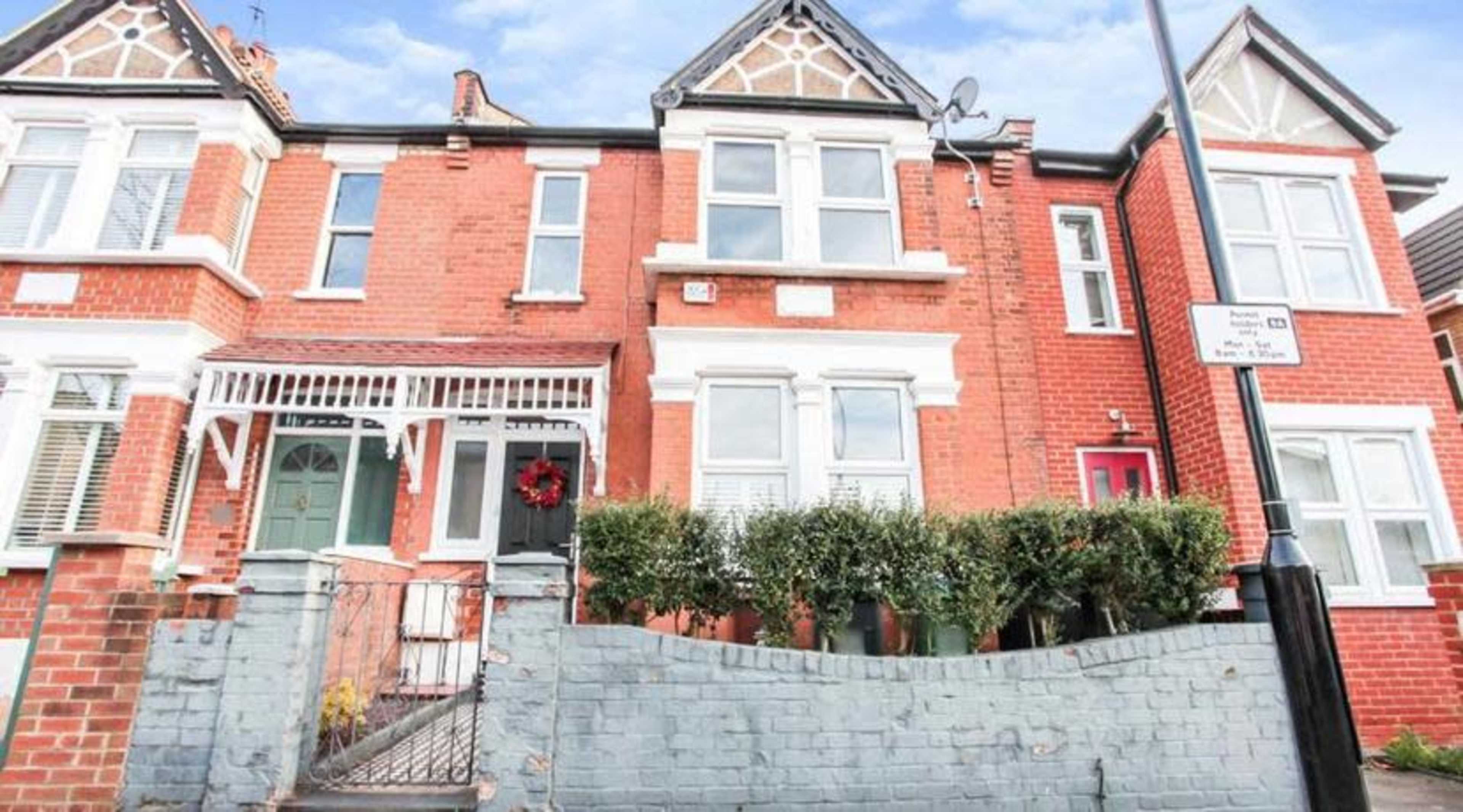 The image shows a row of brick townhouses with decorative gables and a front garden enclosed by a low wall.