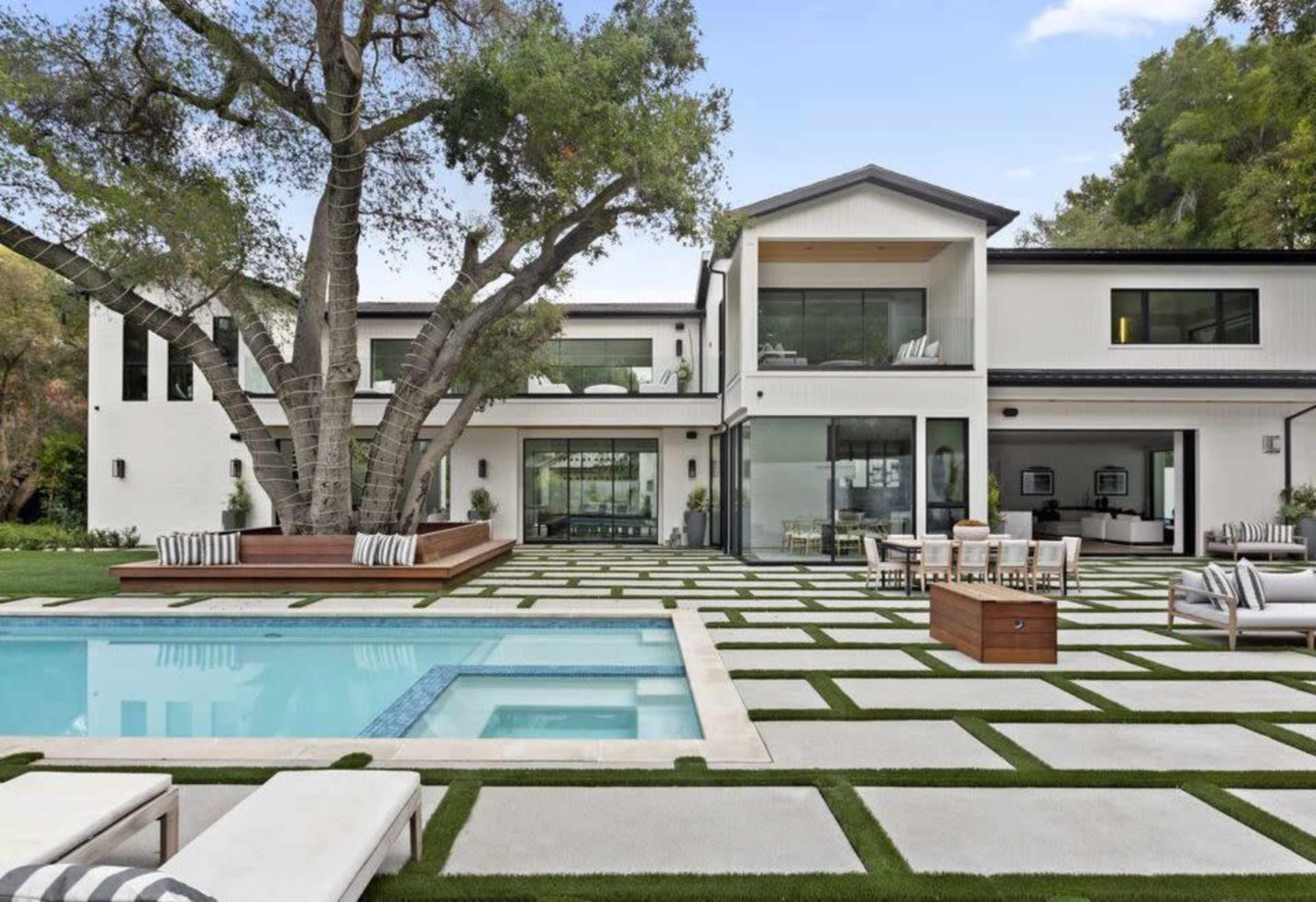 The image shows a modern two-story house with a spacious backyard featuring a swimming pool and a patio area surrounded by geometric grass patterns.