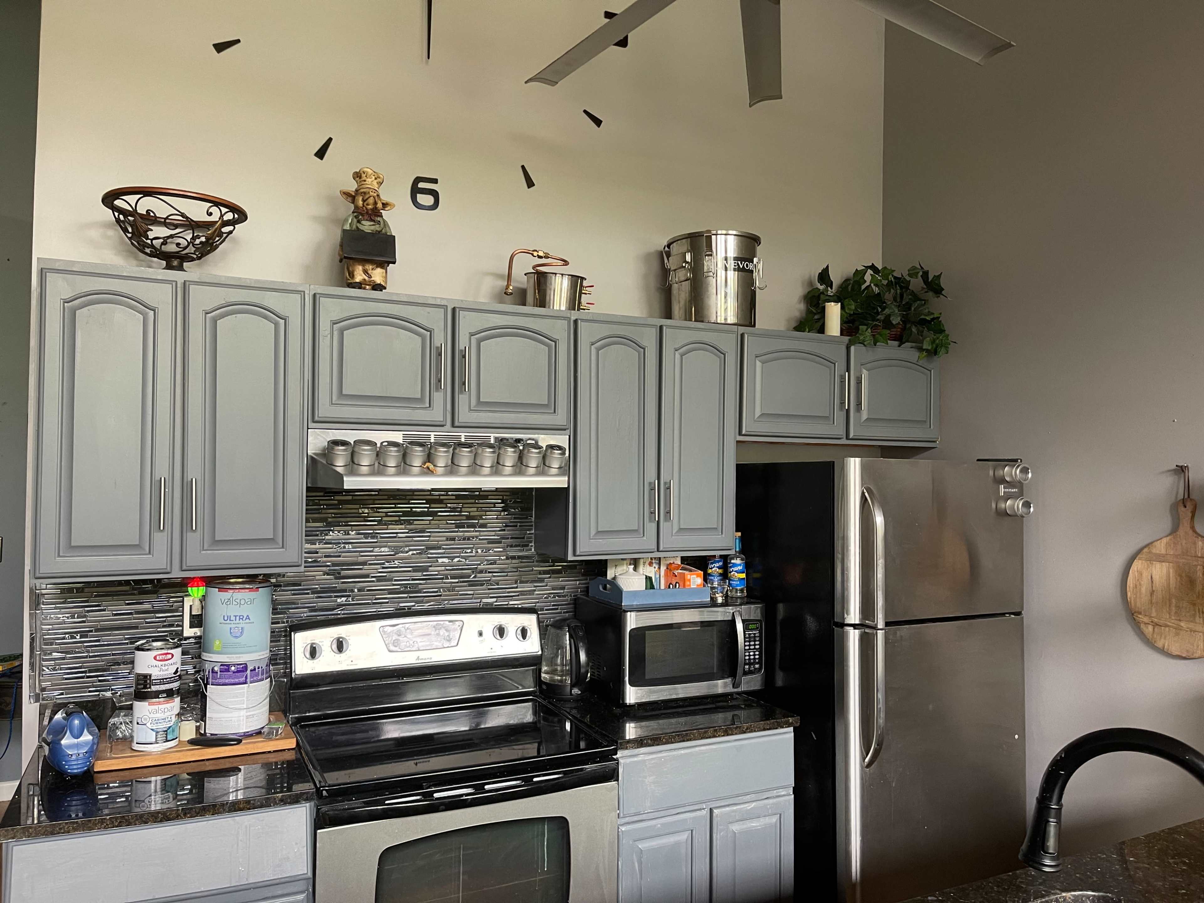 A modern kitchen features gray cabinets, a stainless steel refrigerator, an oven, and various kitchen items on the countertop.