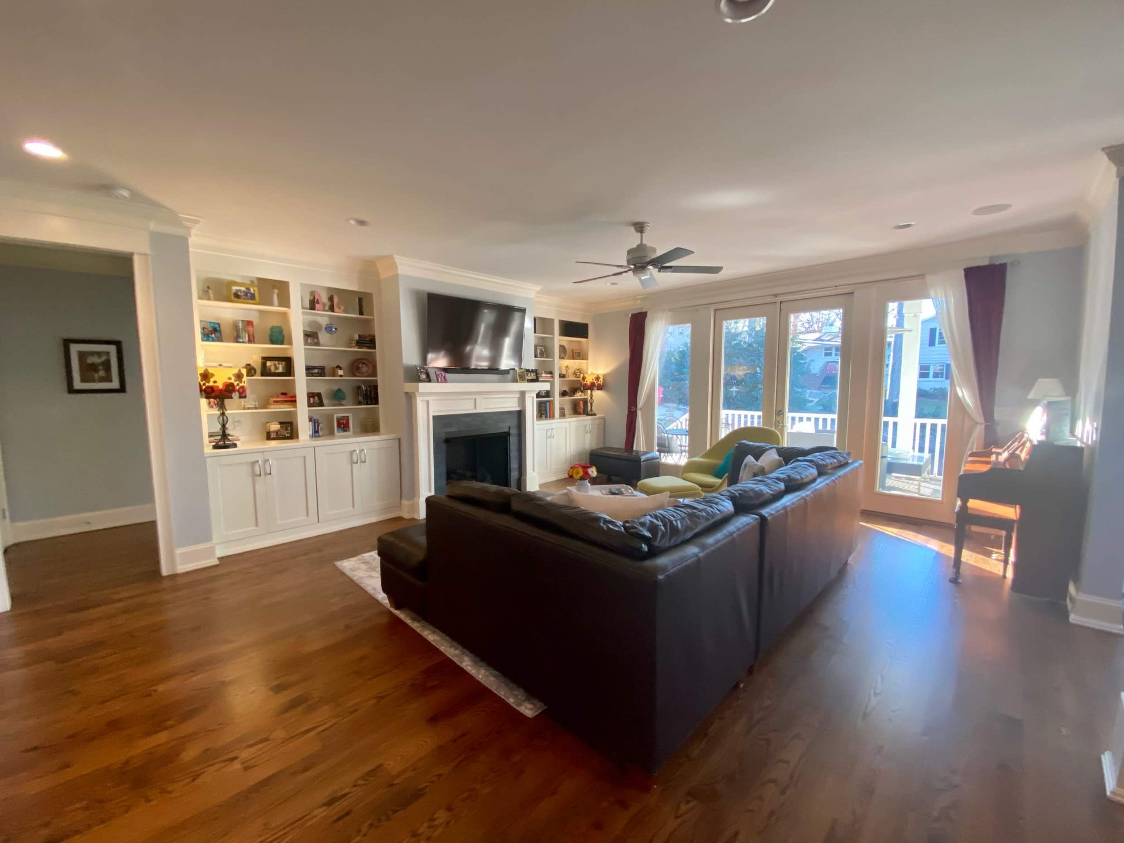 A spacious living room featuring a dark leather sectional sofa, a large television mounted above a white mantel, and built-in shelves displaying various decorative items.
