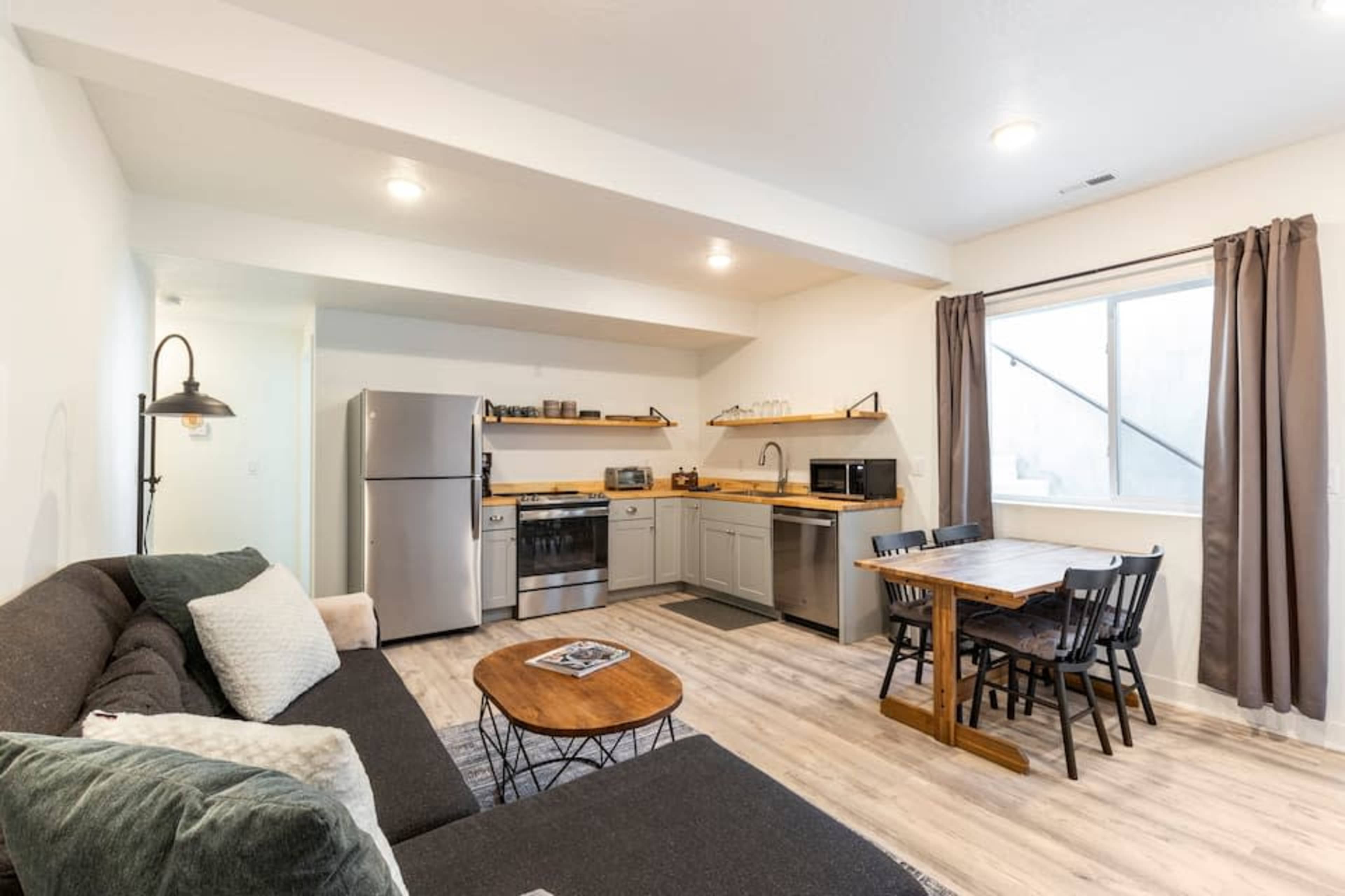A modern living space featuring a kitchen area, a dining table with six chairs, a couch, and a refrigerator.