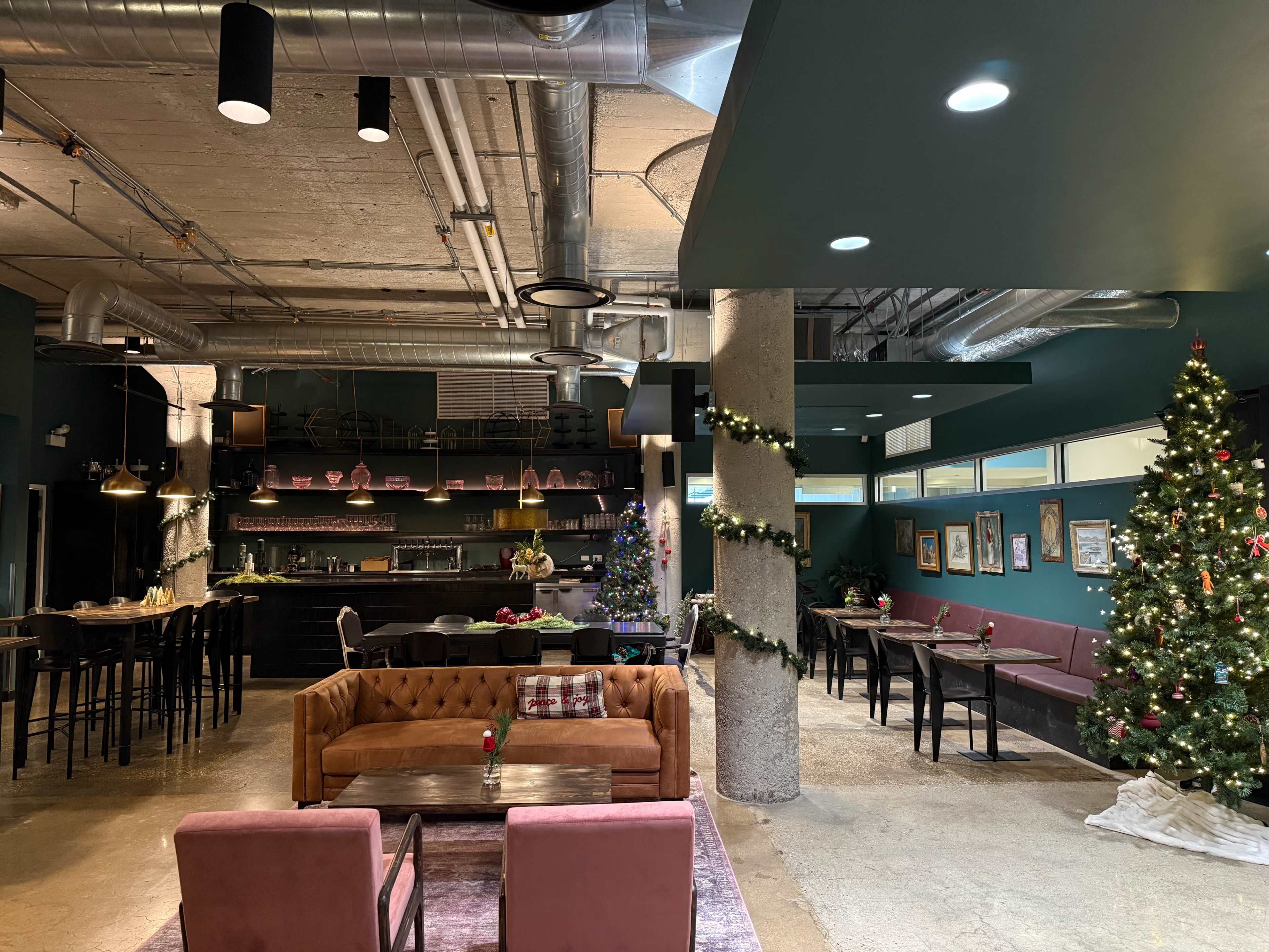 The image shows a festive interior of a cafe or restaurant, featuring a decorated Christmas tree, seating areas with couches and tables, and holiday decorations on the walls.