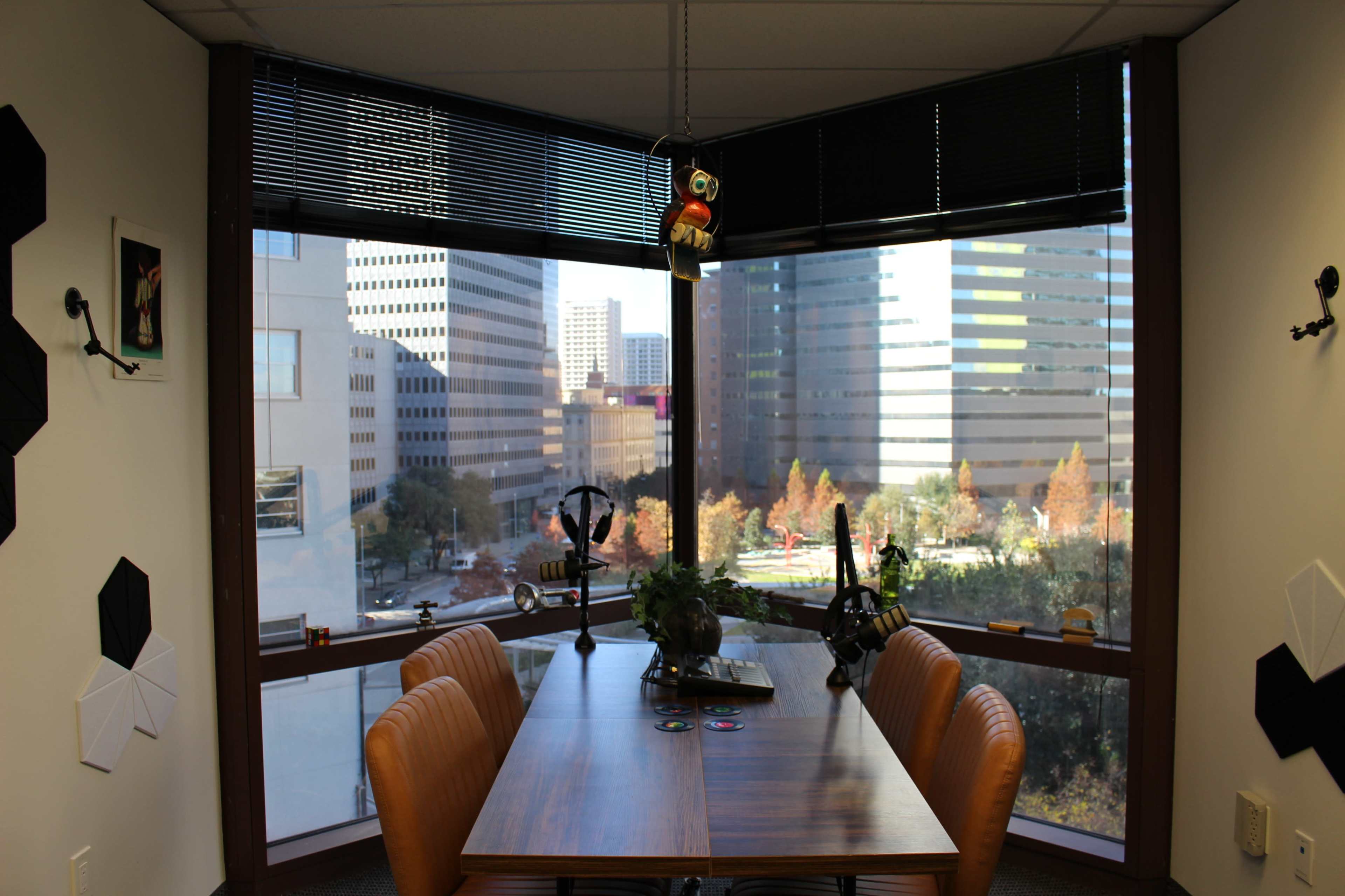 A conference room with a wooden table and leather chairs features large windows displaying a cityscape and a decorative figure hanging from the ceiling.